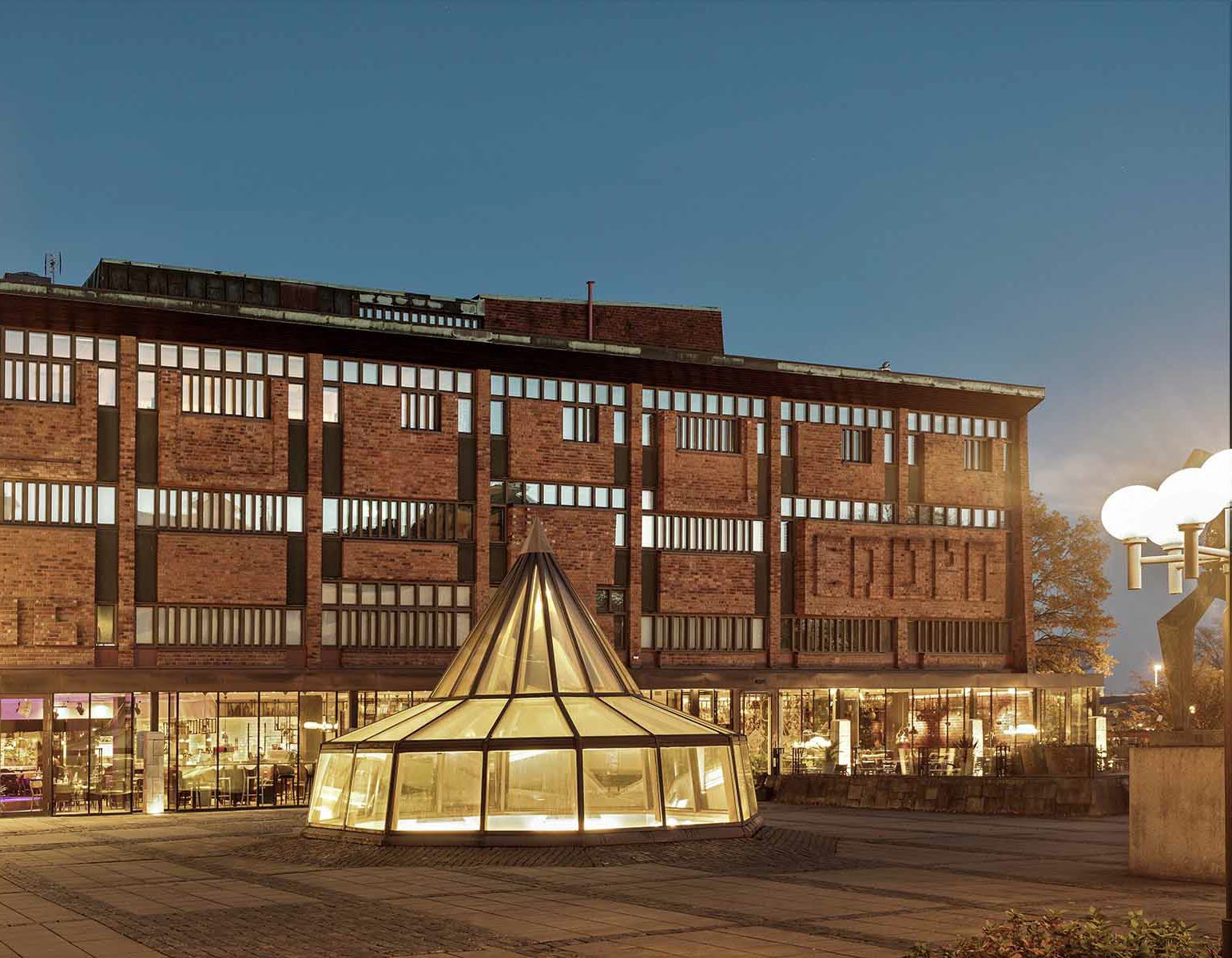 Skövde Kulturhus i kvällsskrud. Från alla fönster i tegelhuset lyser ett varmt gult ljus. 