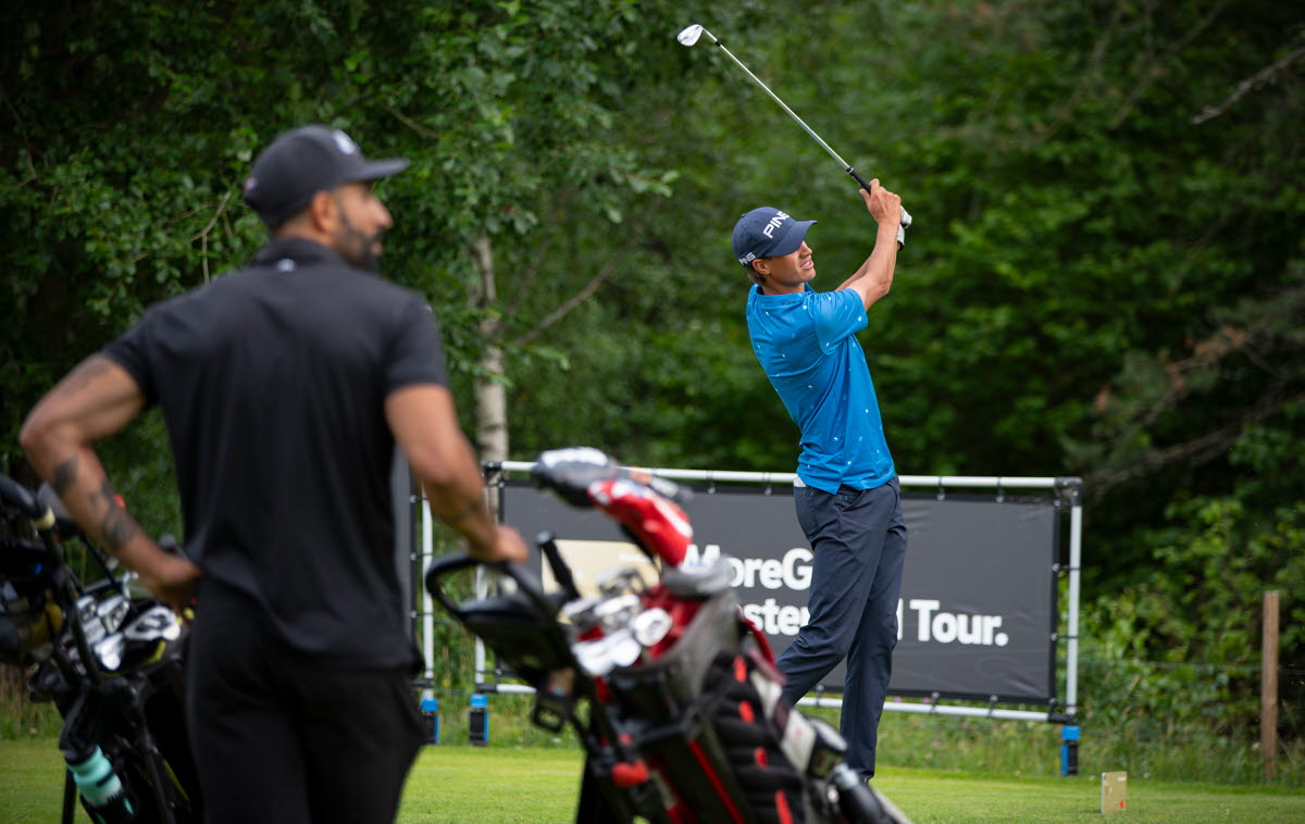 Två män spelar golf. En som svingar en klubba och en som står och tittar på. 