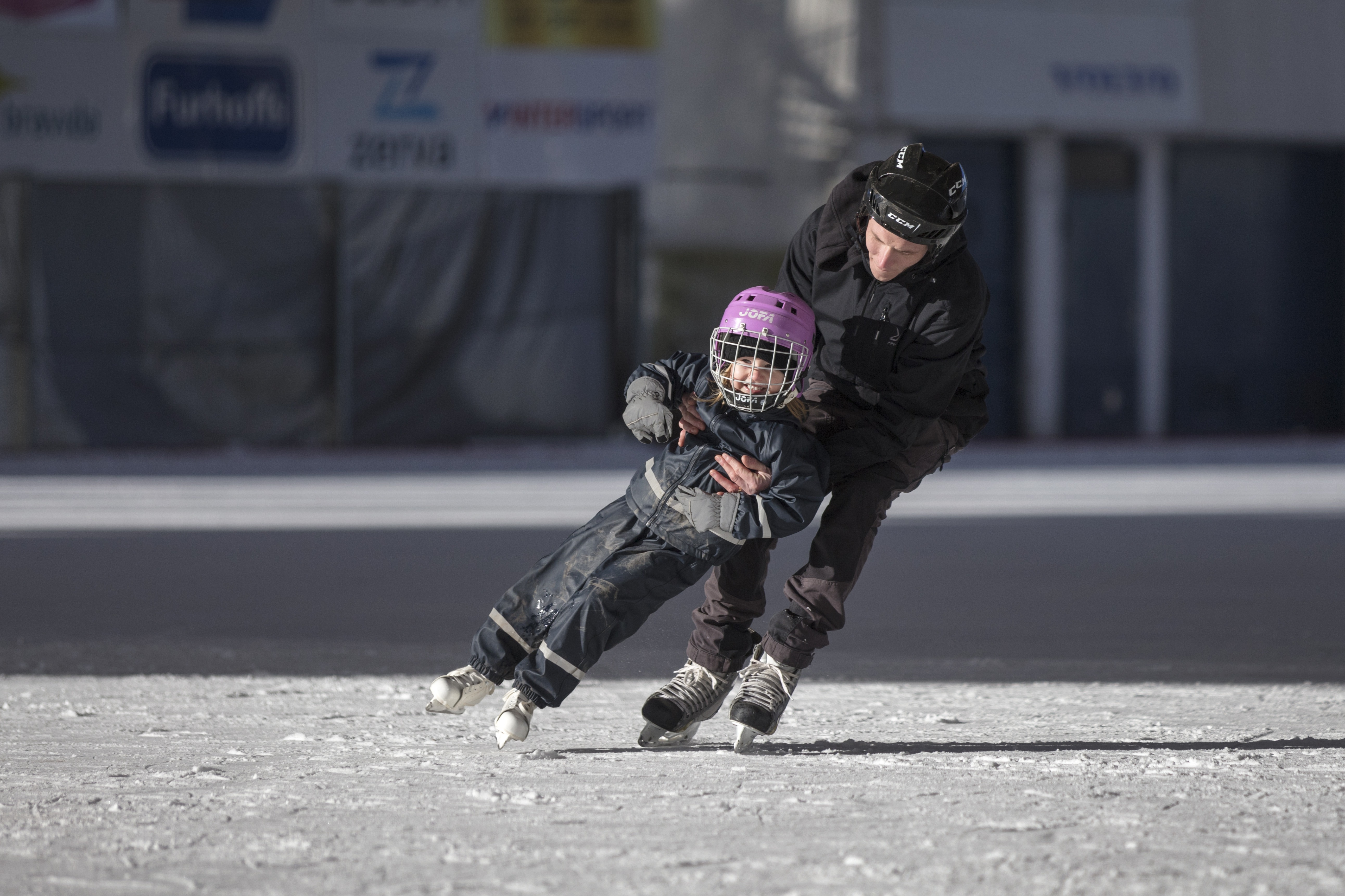 En man åker skridskor och håller ett barn som åker framför honom.