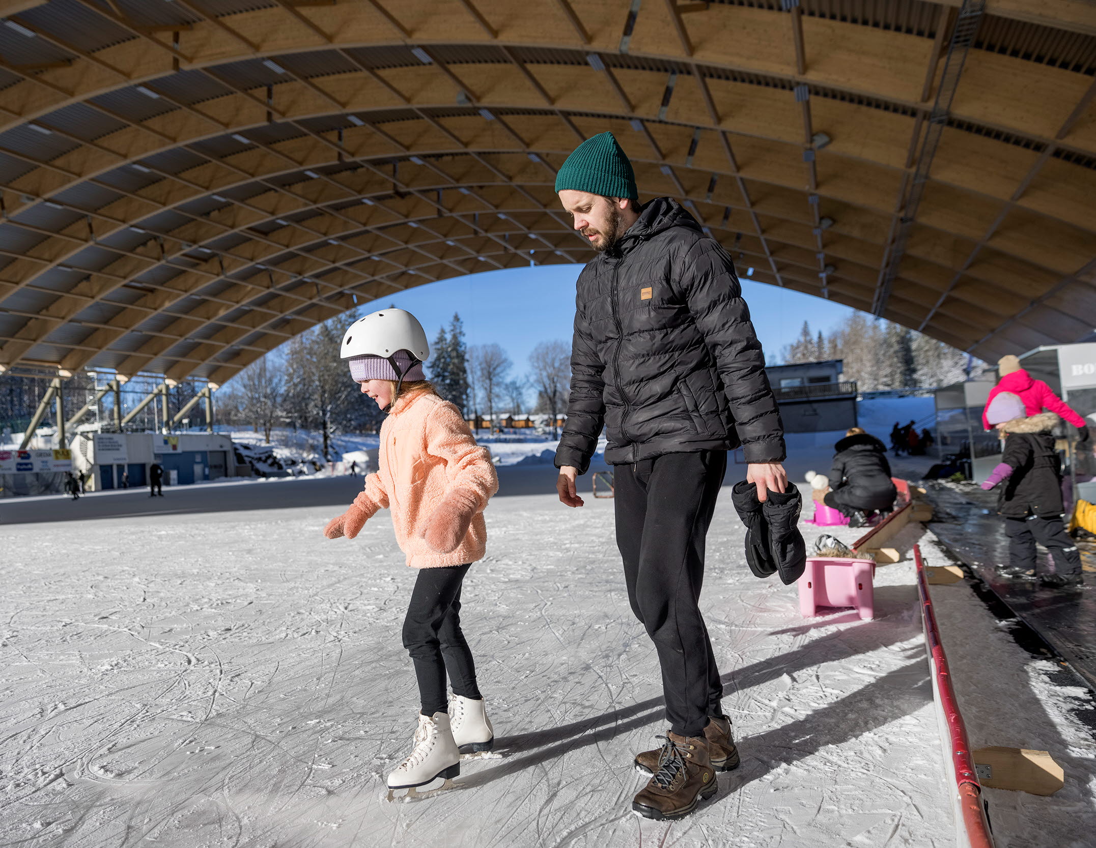 A girl i skating on an ice rink and gets some help from a man.