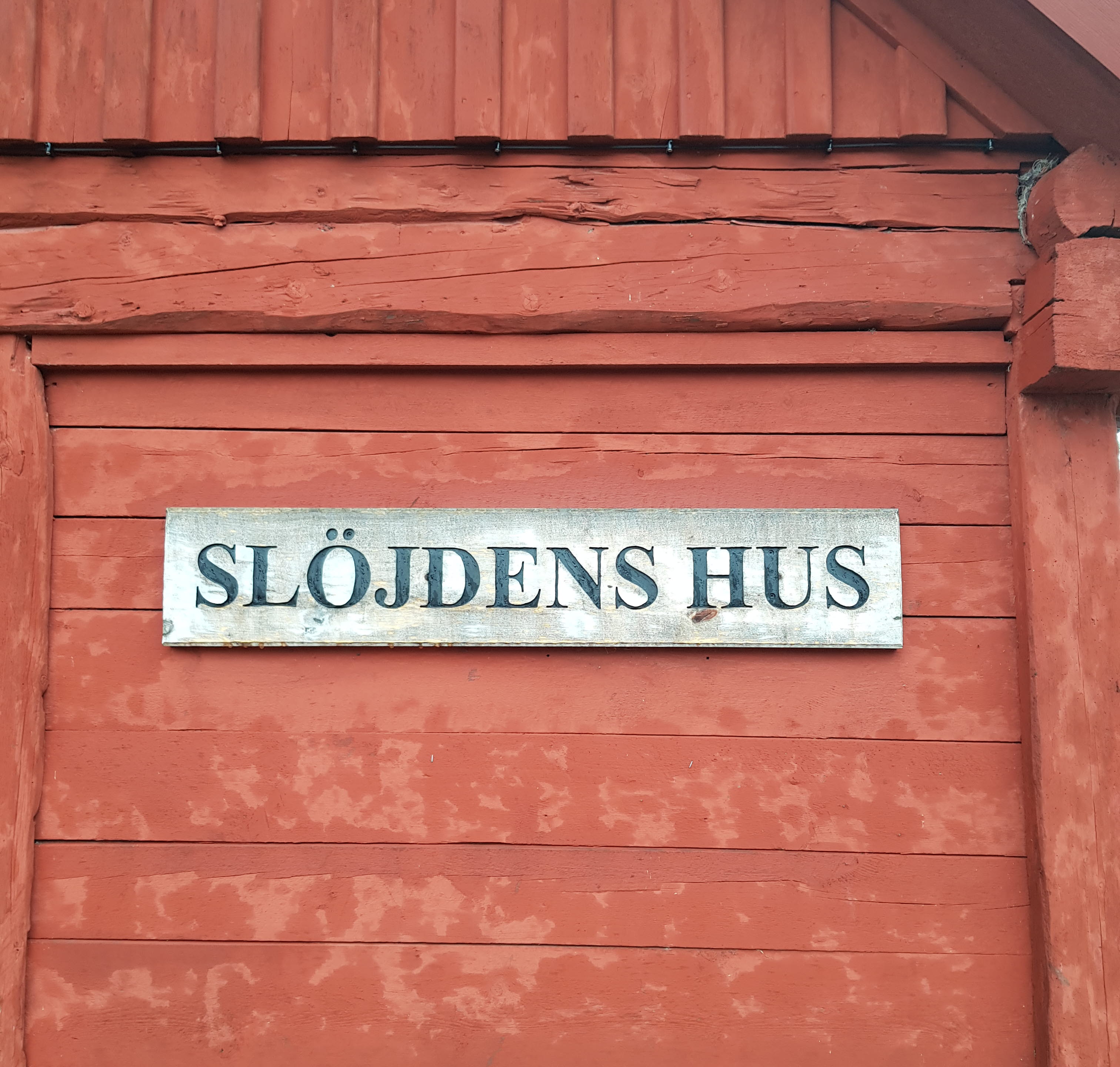 En vägg på en timrad röd stuga. På en skylt står det slöjdens hus. 