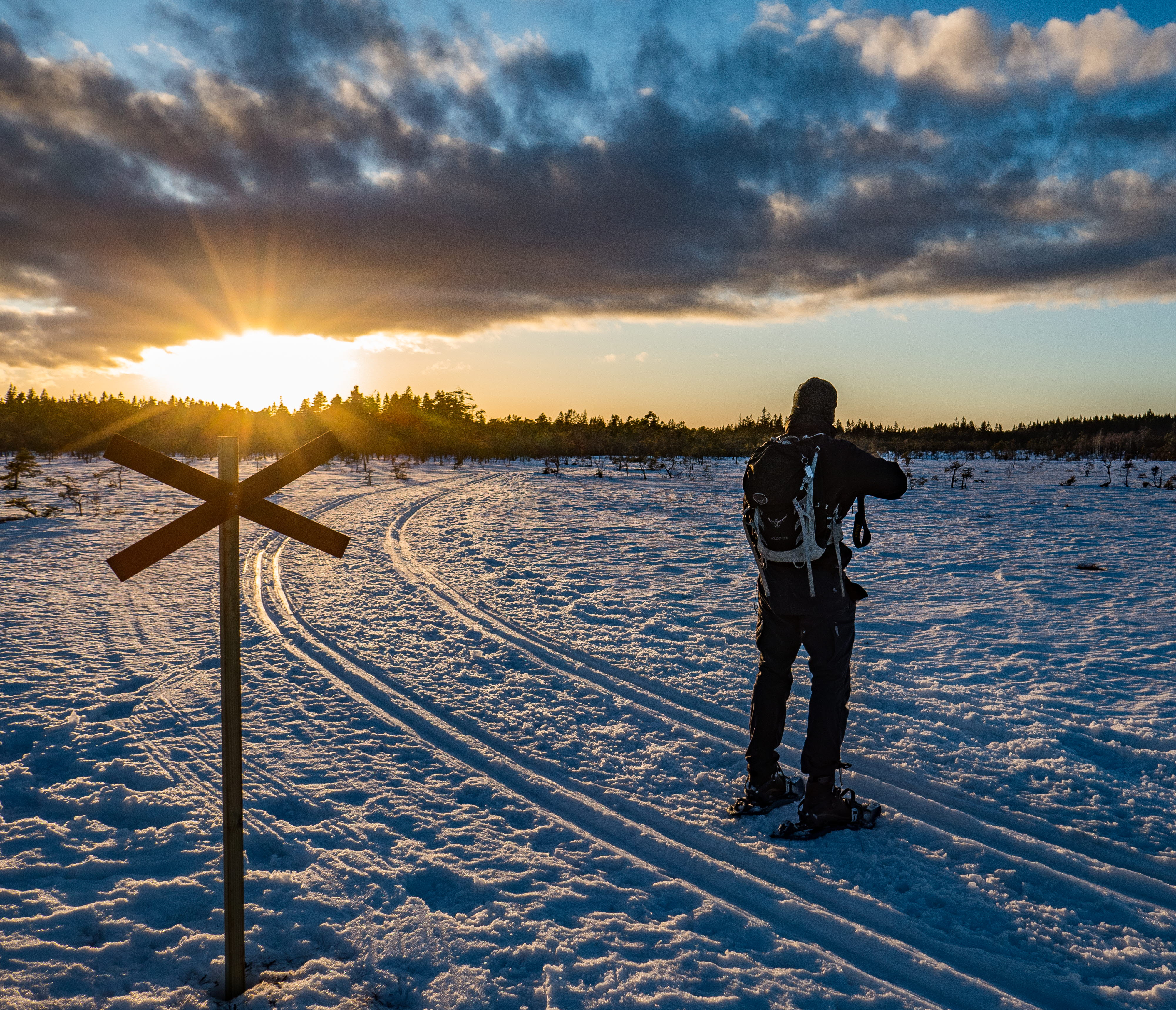 En man i snöskor står i solnedgången och blickar ut över ett snöklätt Blängsmossen. 