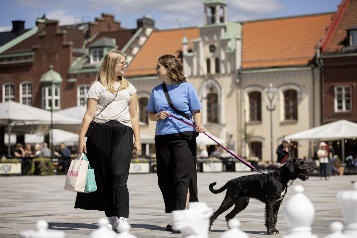 Två tjejer går på torget med en hund.