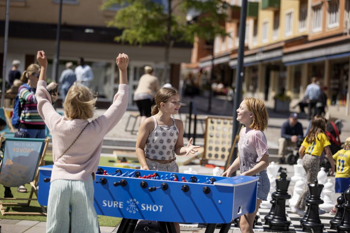 Tre tjejer spelar fotbollsspel på torget. 
