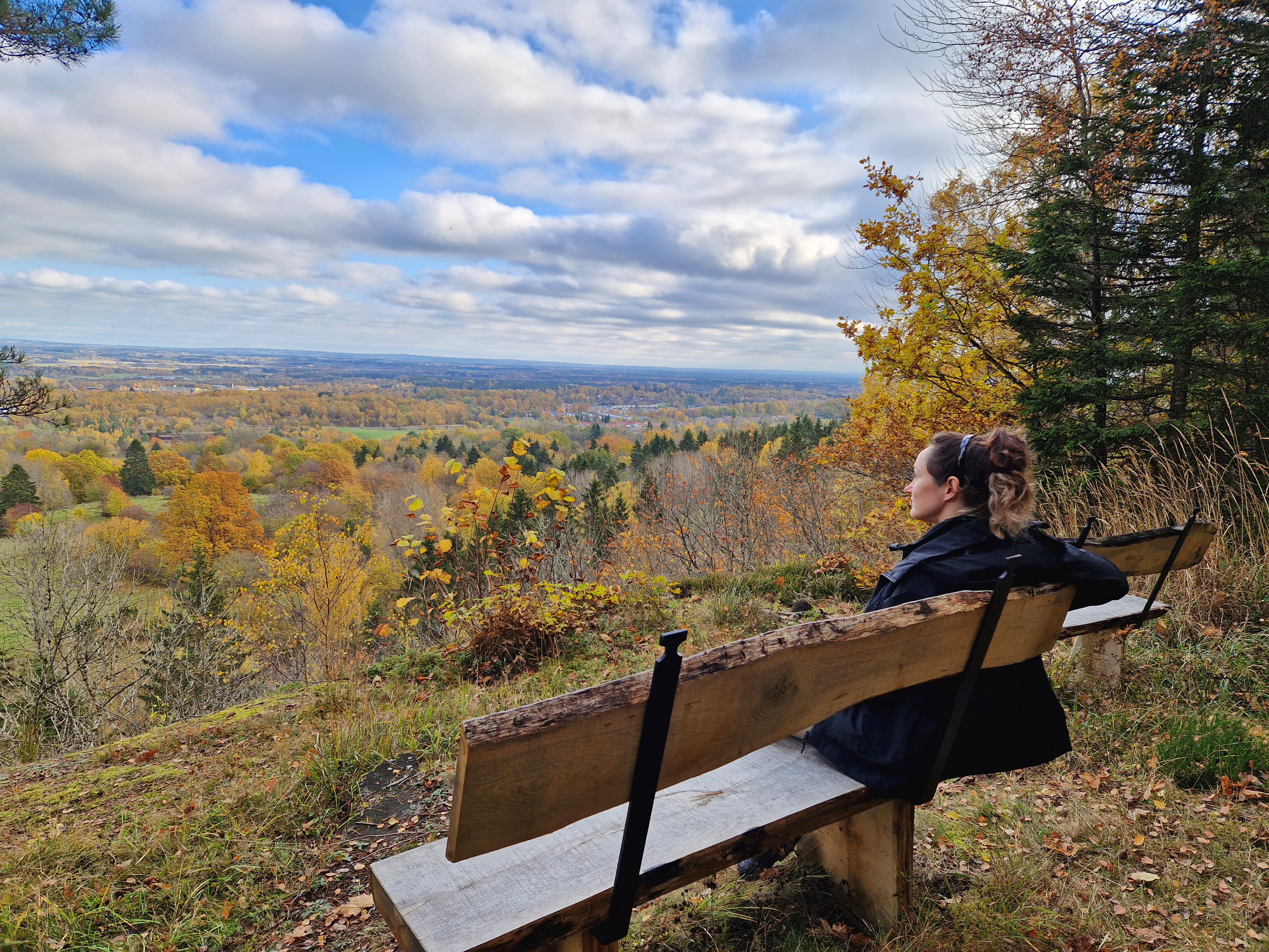 En kvinna sitter på en träbänk vid en bergskanten och njuter av en höstfärgad utsikt. 