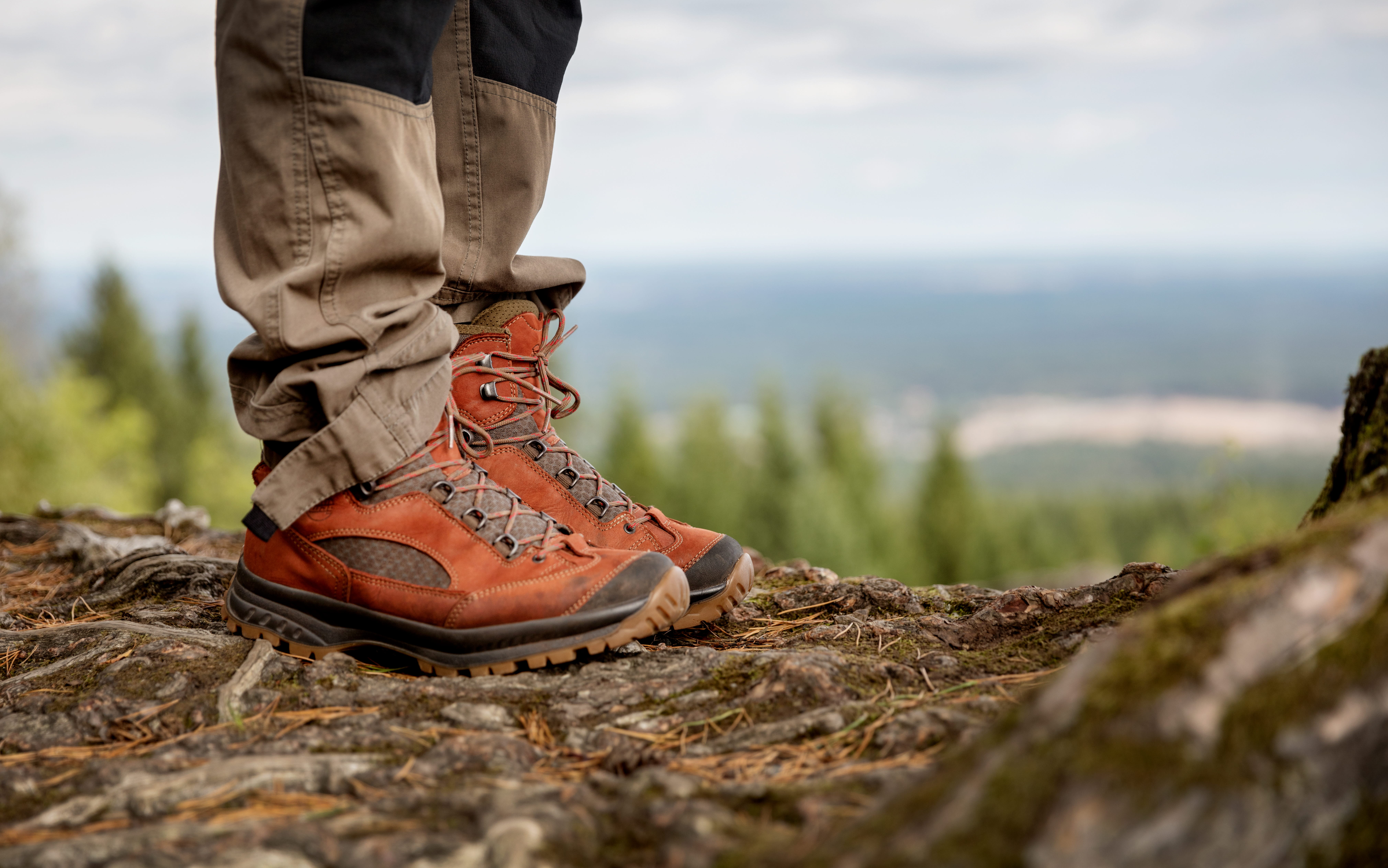 Ben i röda skor ståendes på en klippa med utsikt över skog och vidder