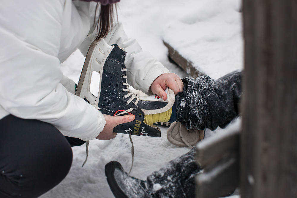 Vuxen hjälper ett barna att knyta skridskor vid isbanan utomhus