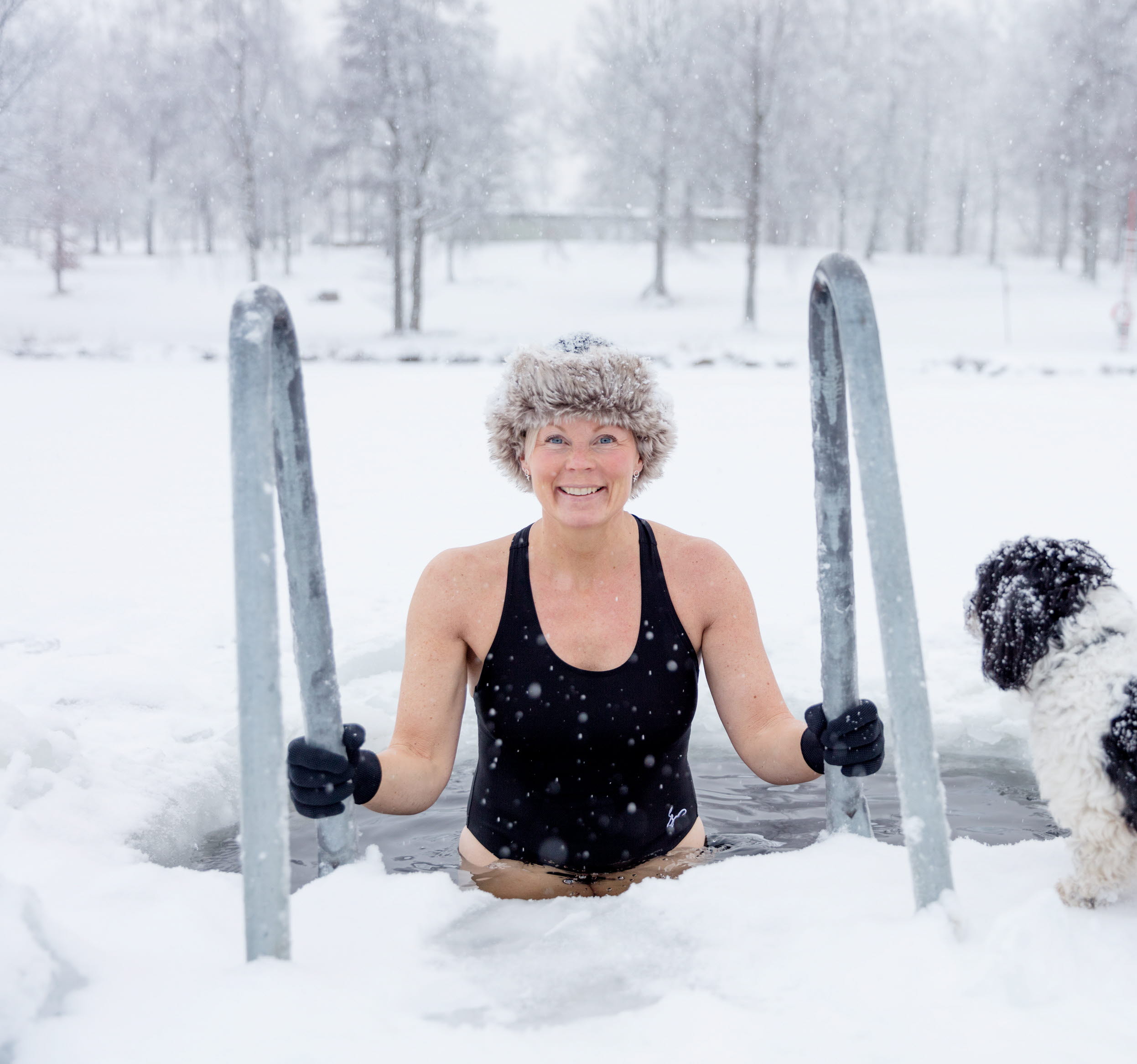 Vinterbadare påväg ned i isvak omgiven av ett snöigt vinterlandskap vid Simsjön i Skövde. 