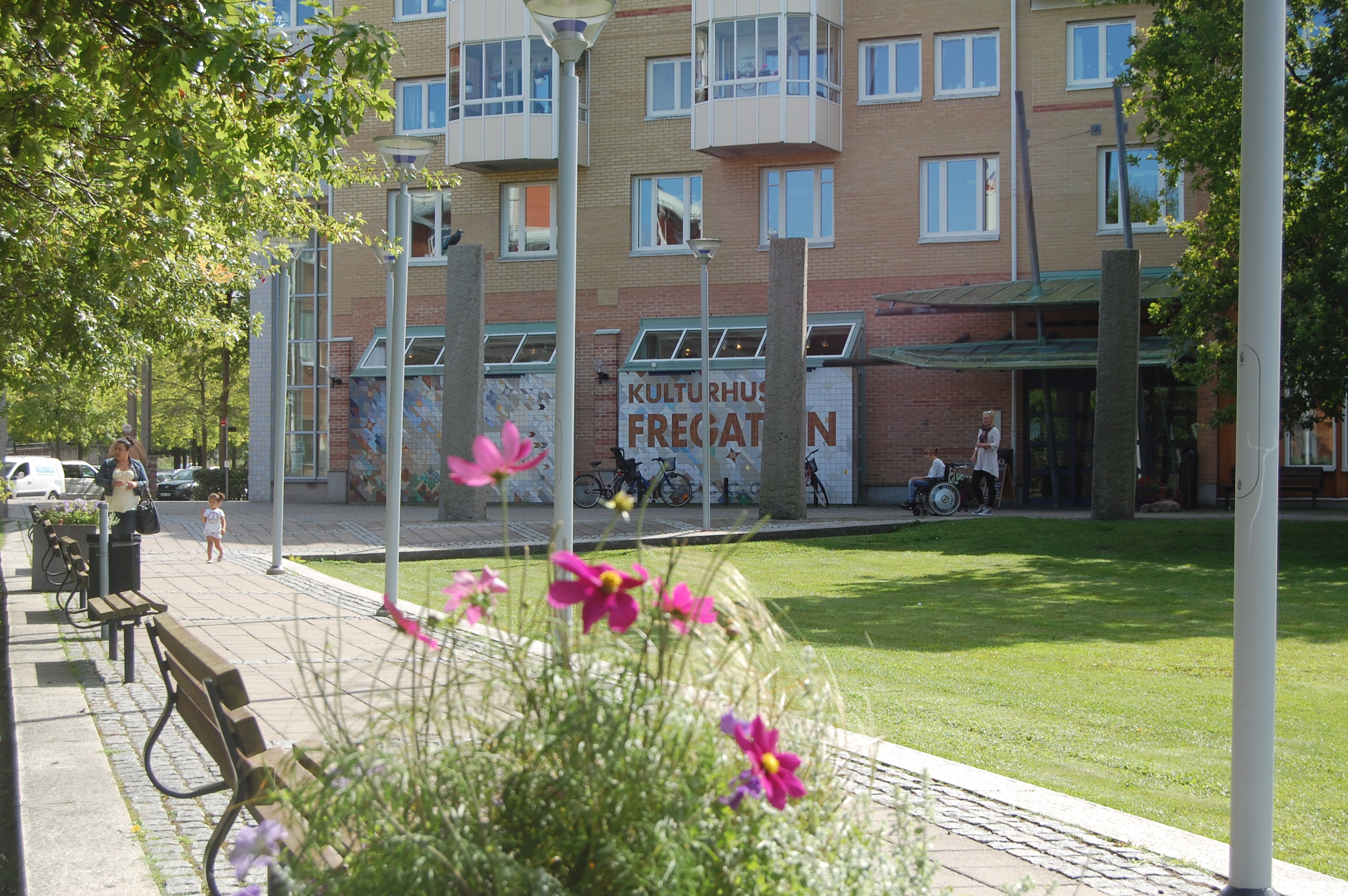 Foto från utsidan av Kulturhuset Fregatten med en del av parken och blommor.