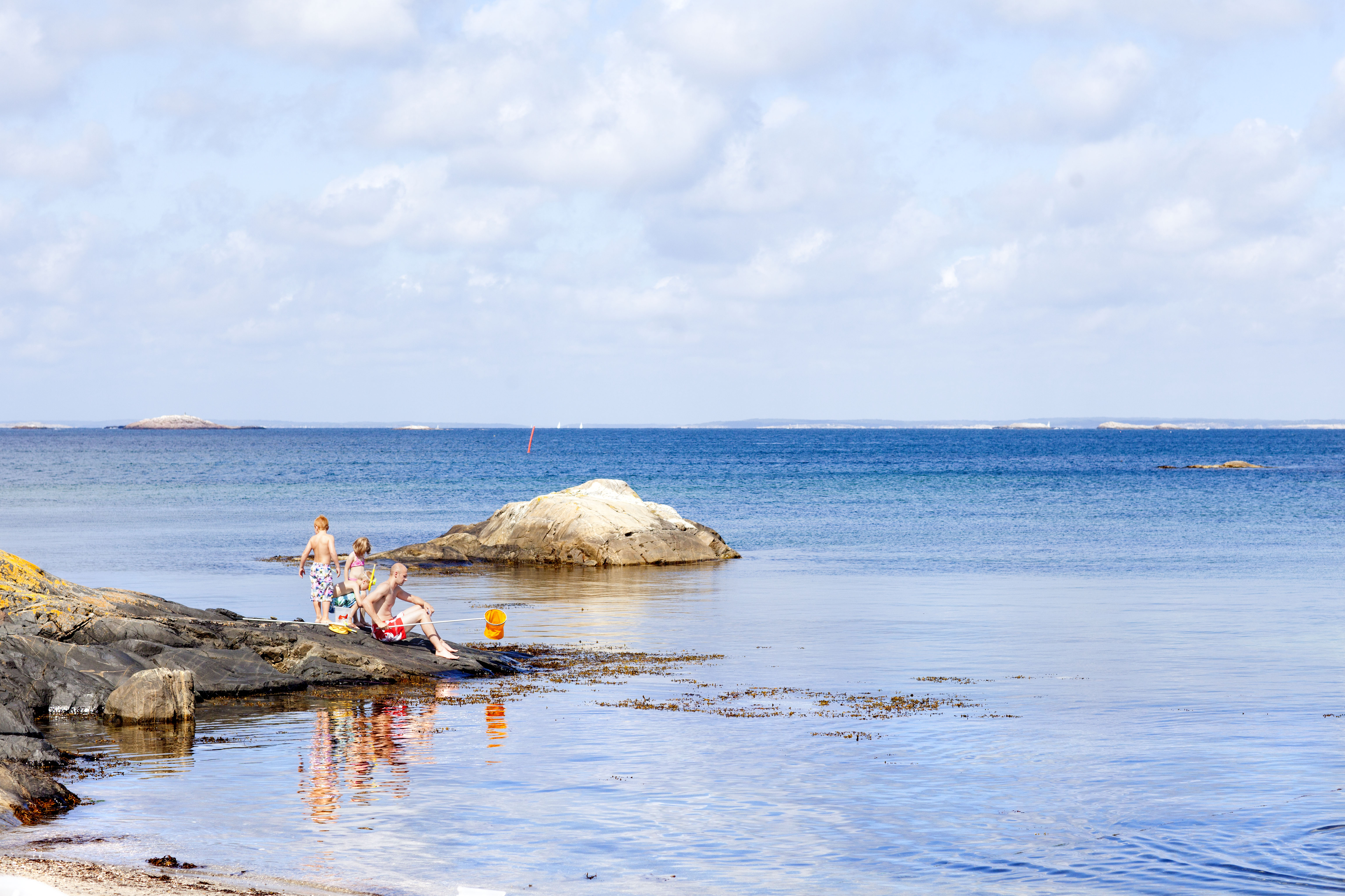 It's a sunny summer's day and a family with kids are fishing crabs from a cliff at Rörvid, South Koster. 