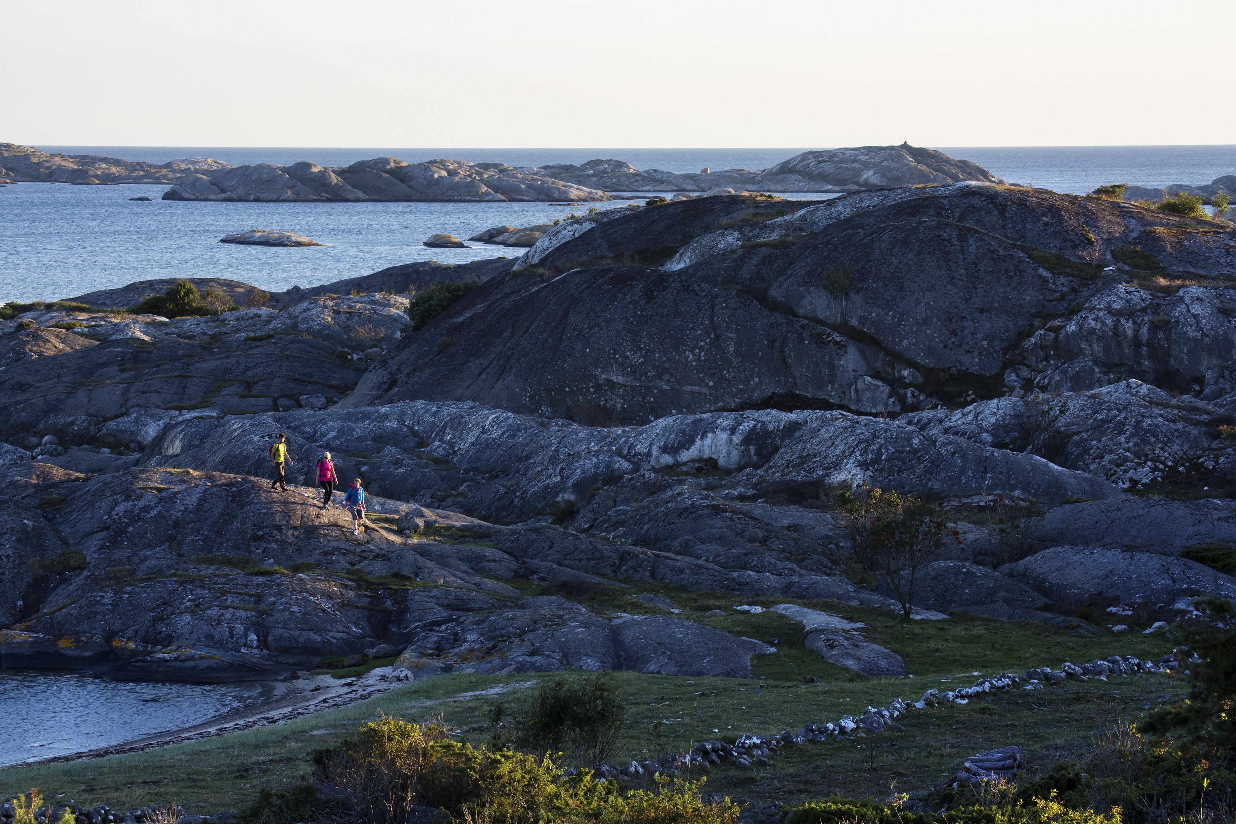 Three paople are hiking along a large cliff at North Koster. 