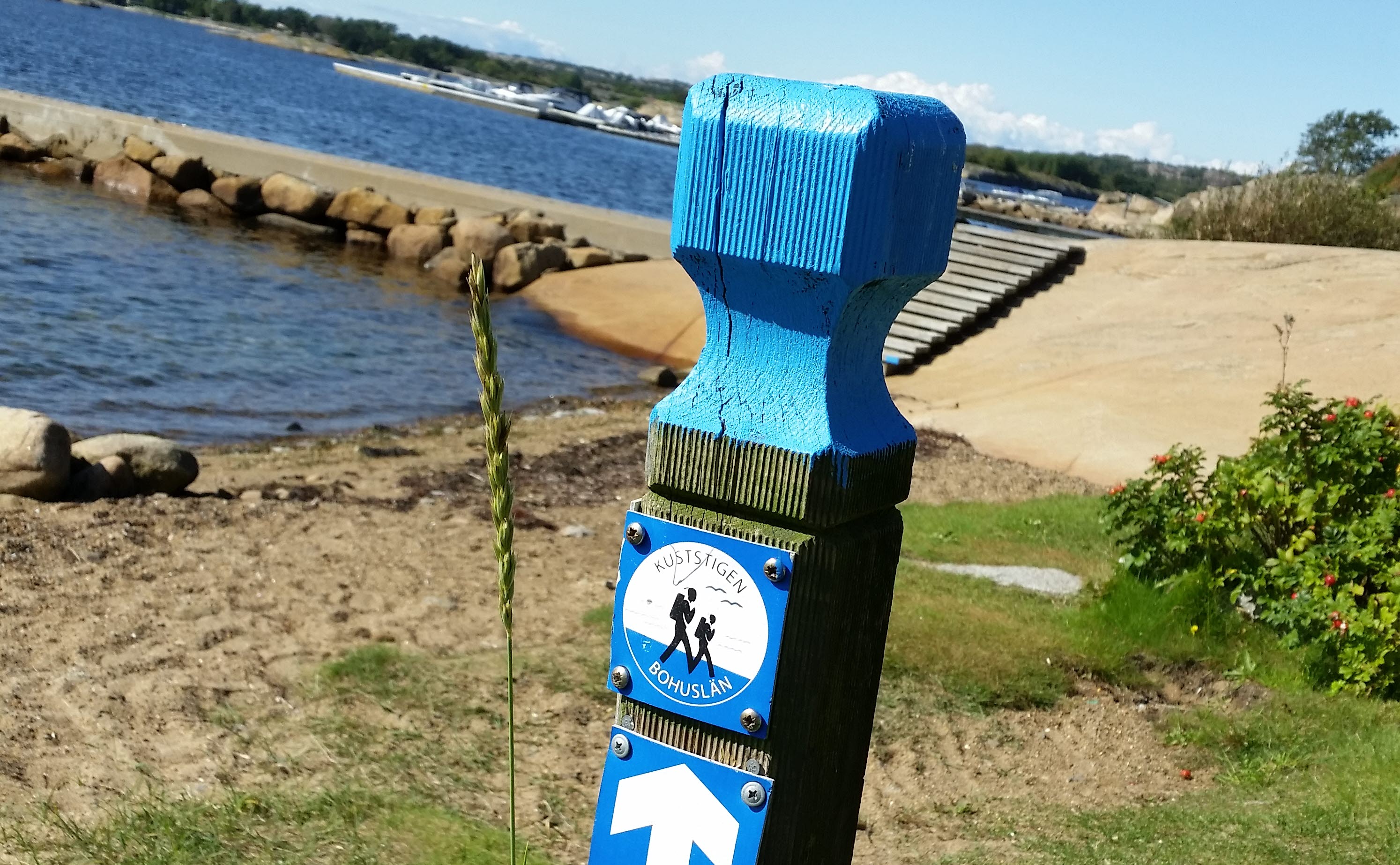 Vandringsled Kuststigen, markör på stolpe vid havet. 