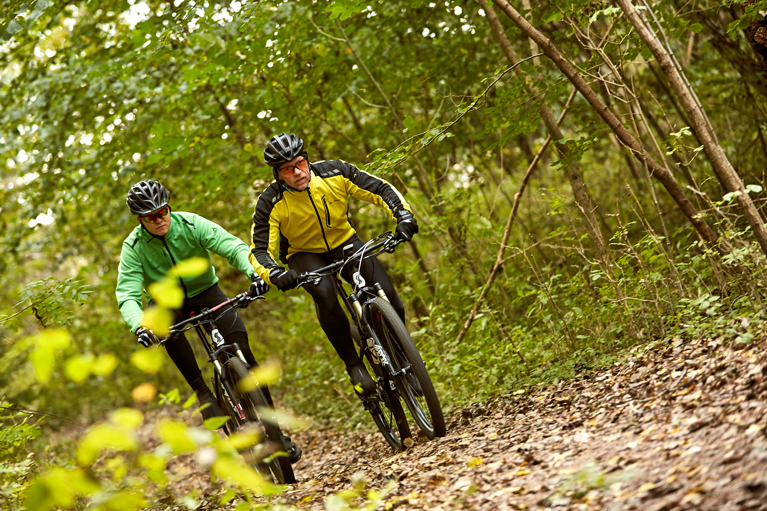 Två mountainbikcyklister cyklar genom lövskog