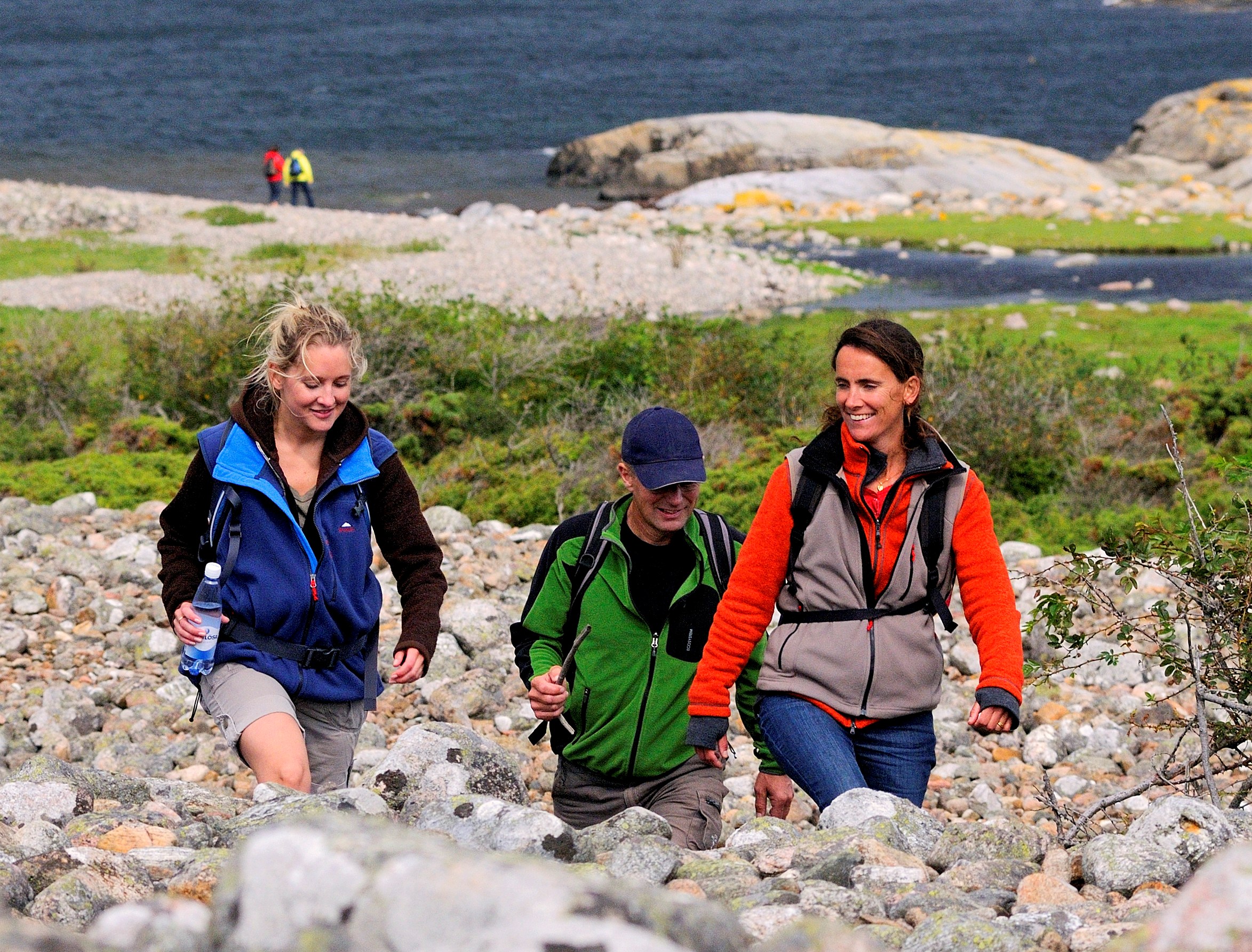 Three people are hiking across a cobblestone field at North Koster. 