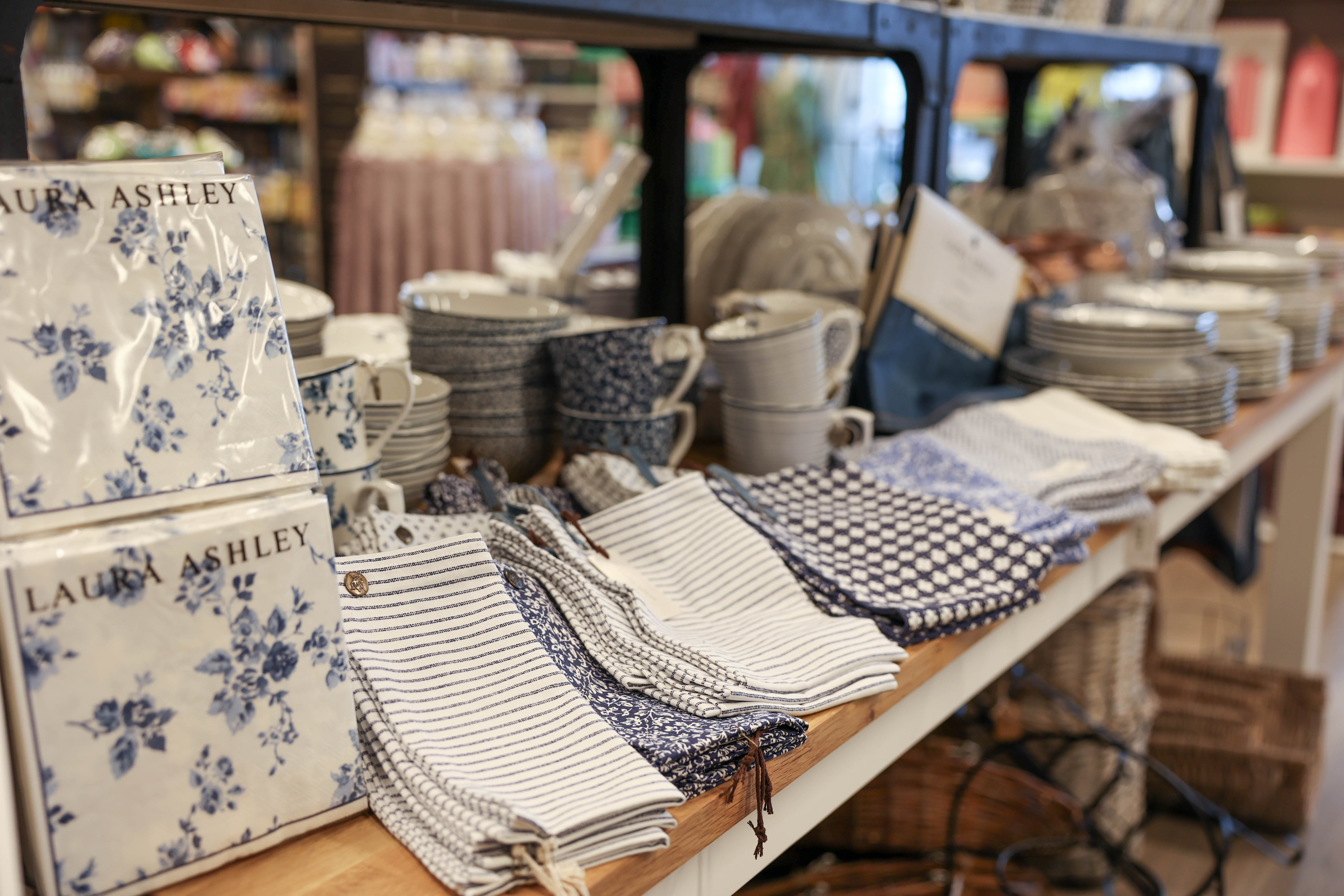 Butikshylla med Laura Ashley-serviser, kökshanddukar och porslin i blåvita mönster.