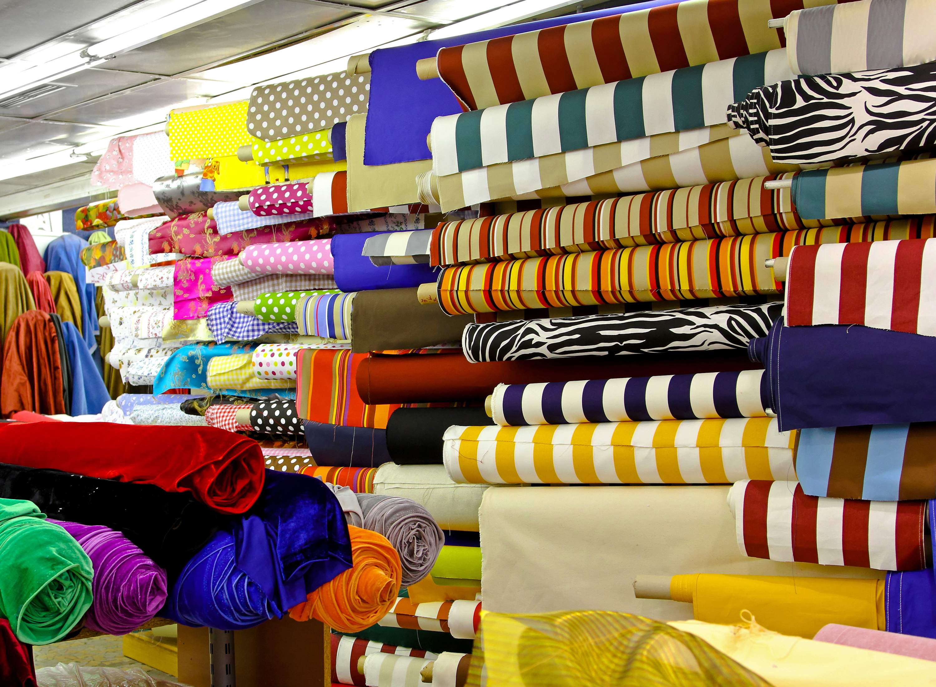Vy över flera rullar med tyger i olika färger i en tygaffär.
