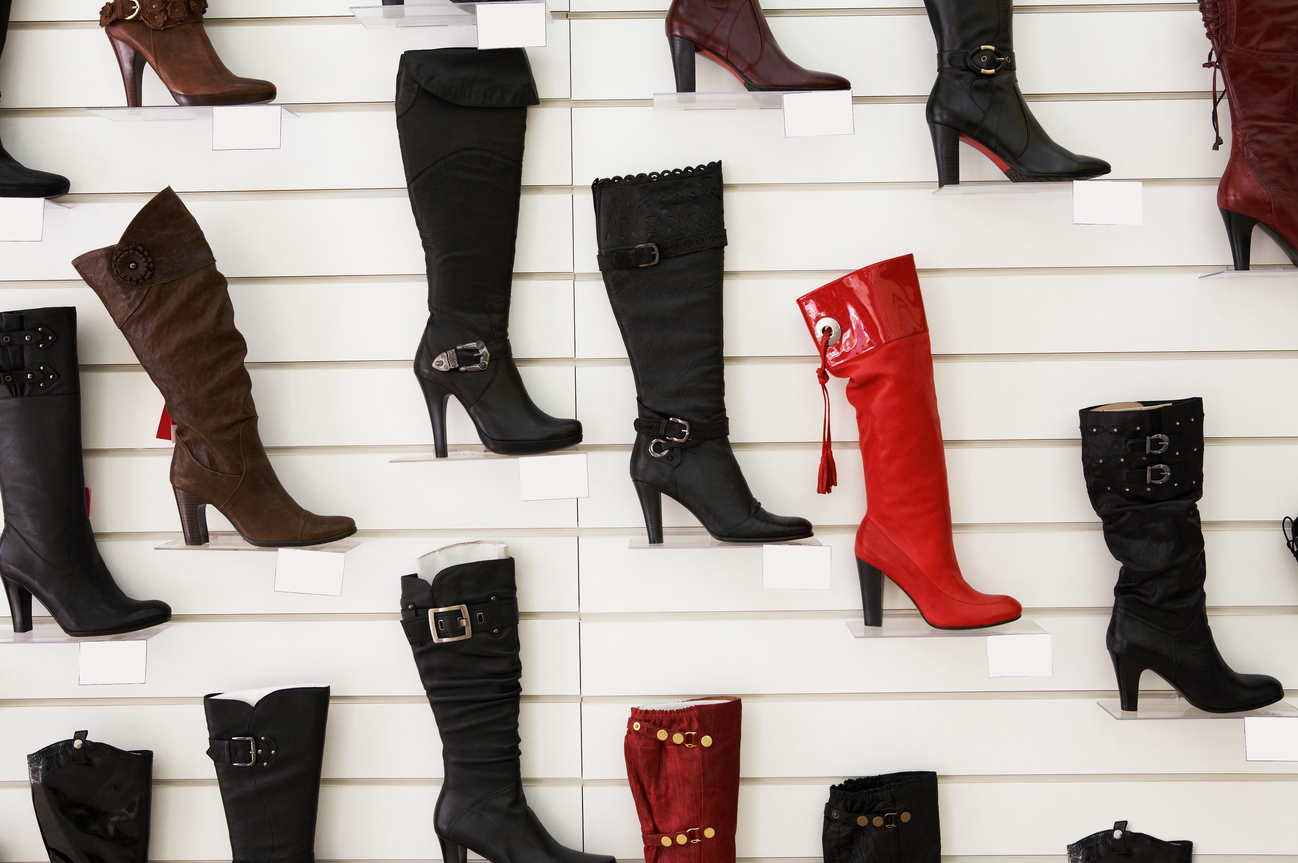 Several fashion boots suspended on a white wall.