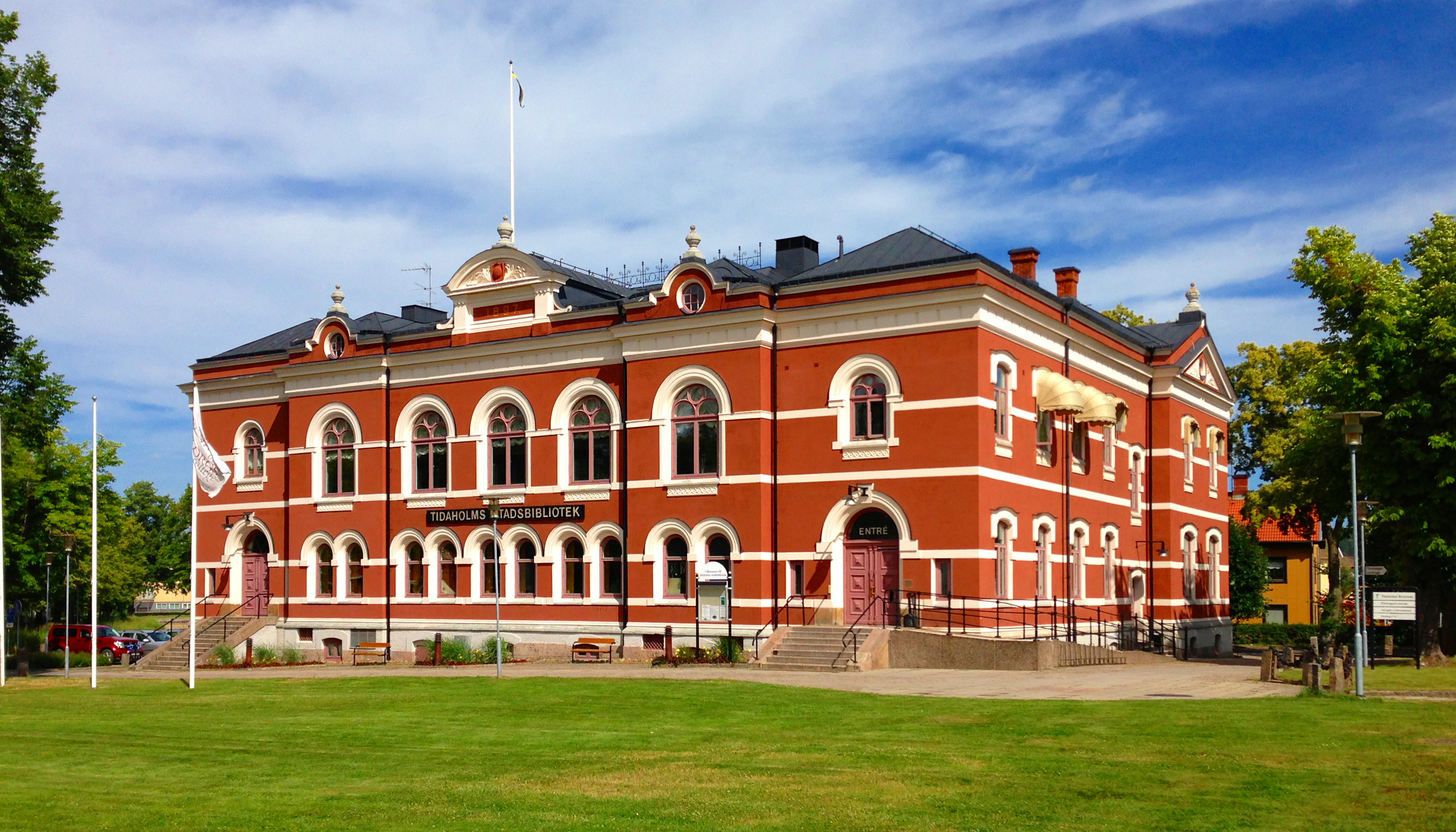Vy över Tidaholms stadsbibliotek en sommardag. Rött stenhus med fina detaljer.