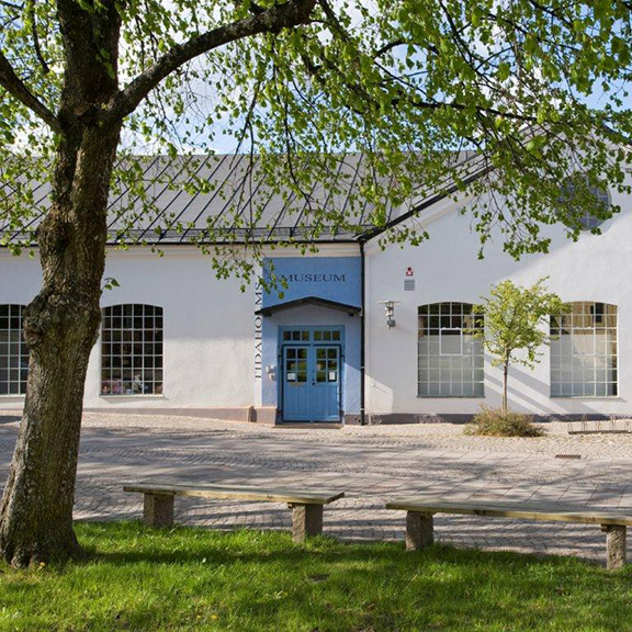 Tidaholms museums entré i sommarskrud med ett träd i förgrunden.