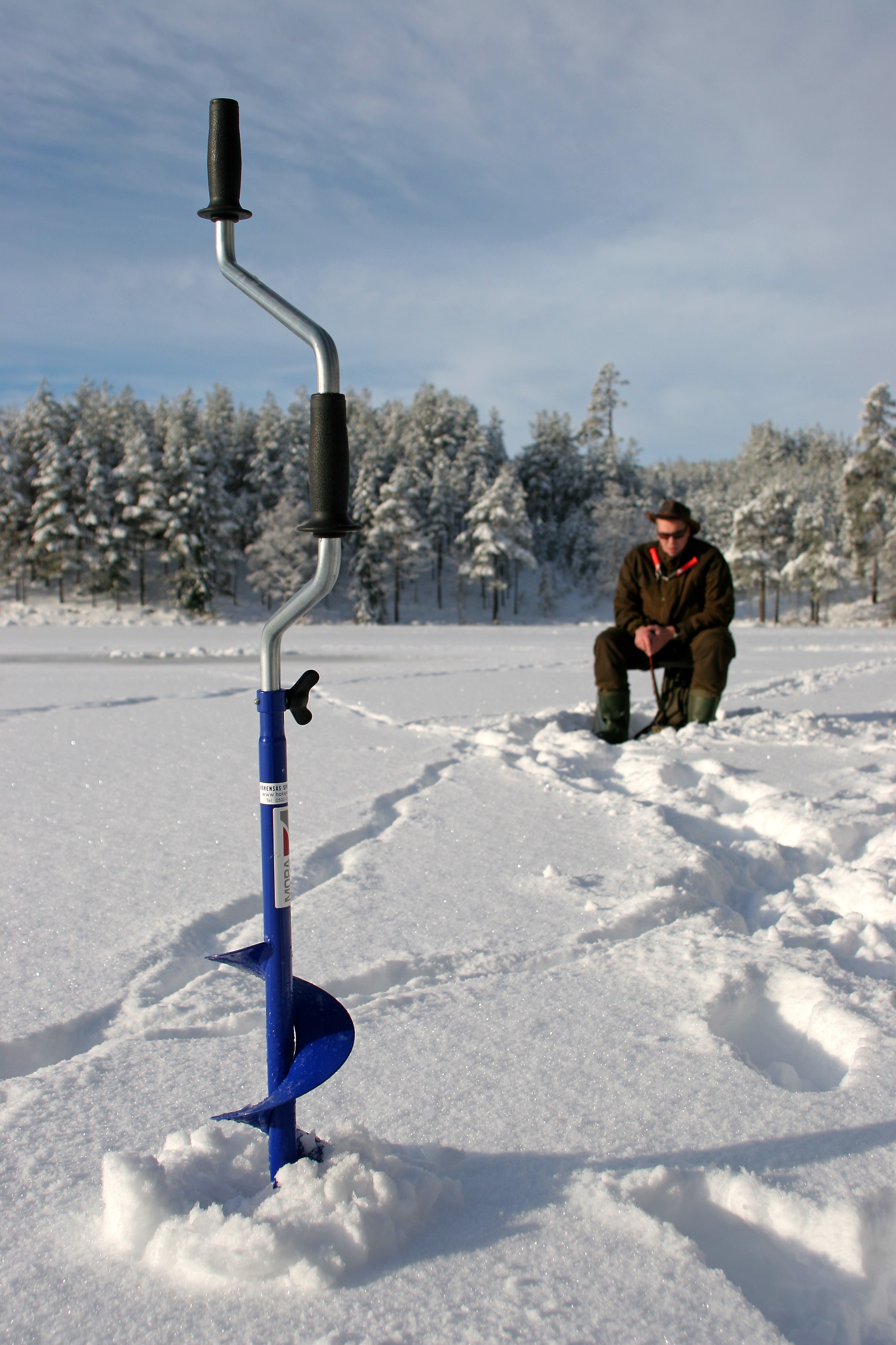 En isborr på en snöig sjö med en man sittandes på en pall bakom.