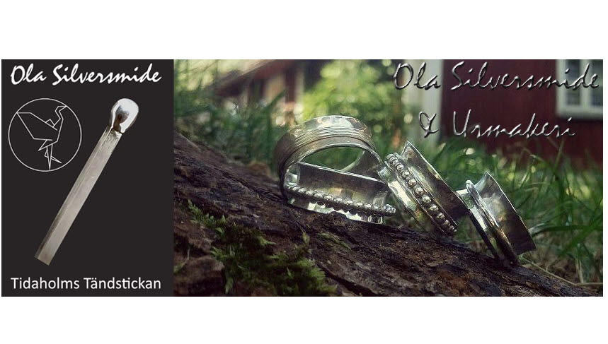 Flera silverringar ligger på en gren med ett litet rött trähus i bakgrunden. Ringarna är gjorda av Ola Silversmide i Tidaholm.