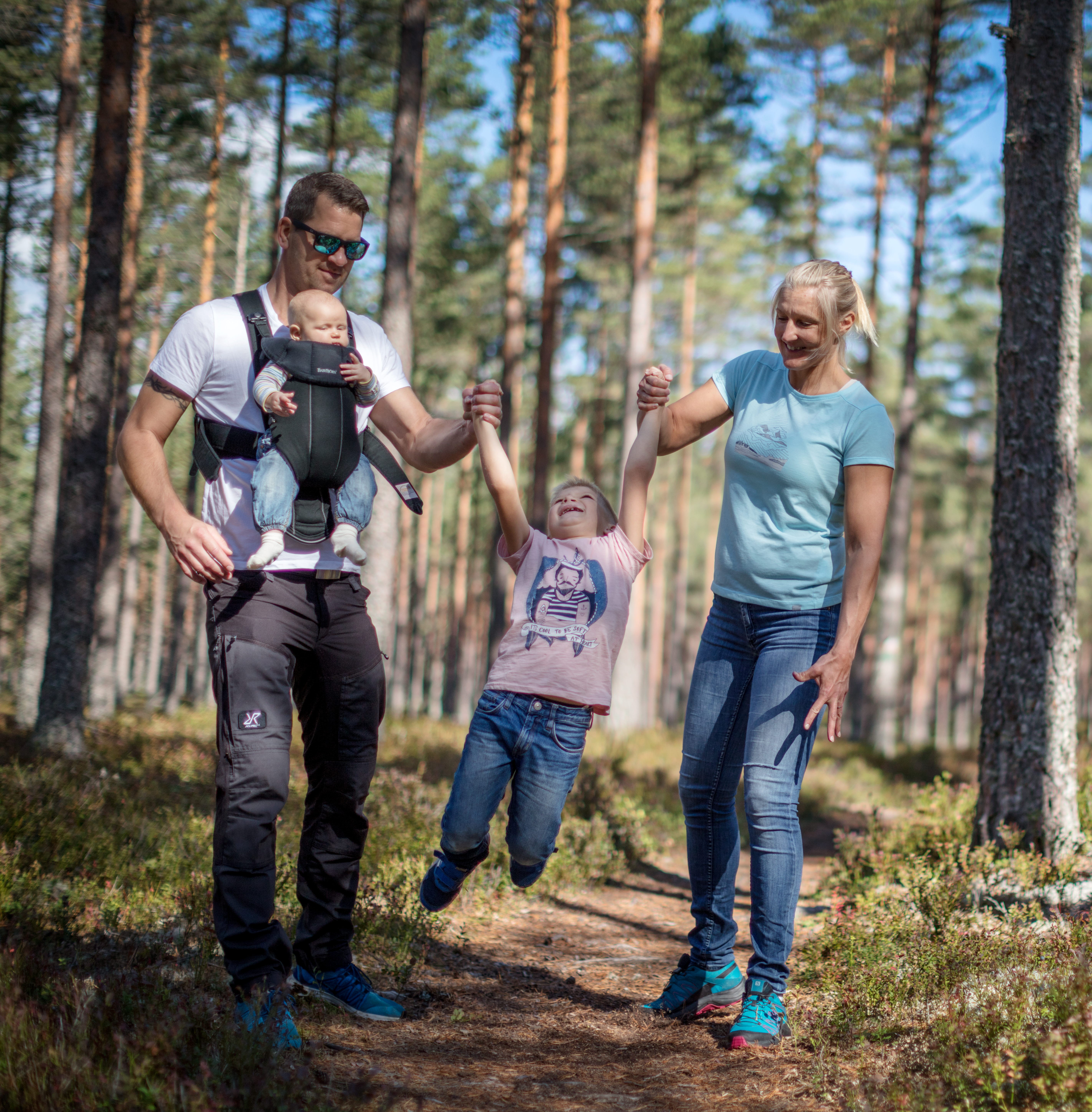 En pappa och en mamma håller sitt barn mellan sig och gungar honom fram och tillbaka. Pappan har ett spädbarn i en sele på magen