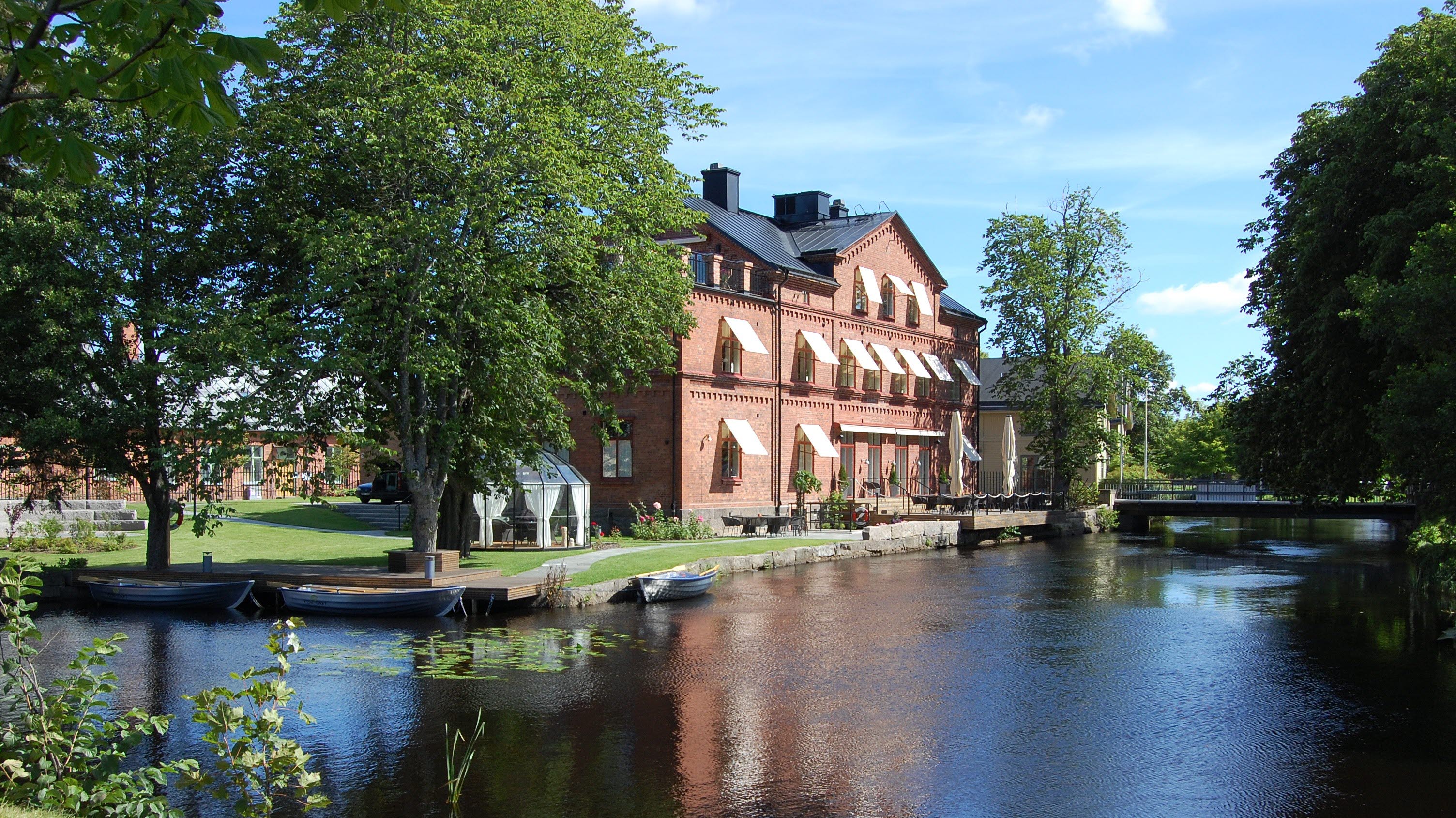 VinContoret som är en restaurang med ån Tidan framför byggnaden. Bilden tagen i sommargrönska.