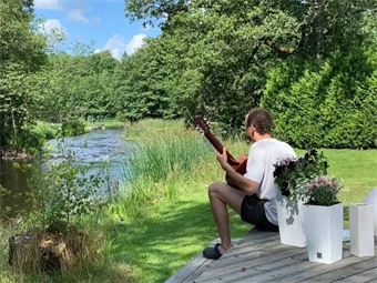 En man sitter på altan och spelar gitarr