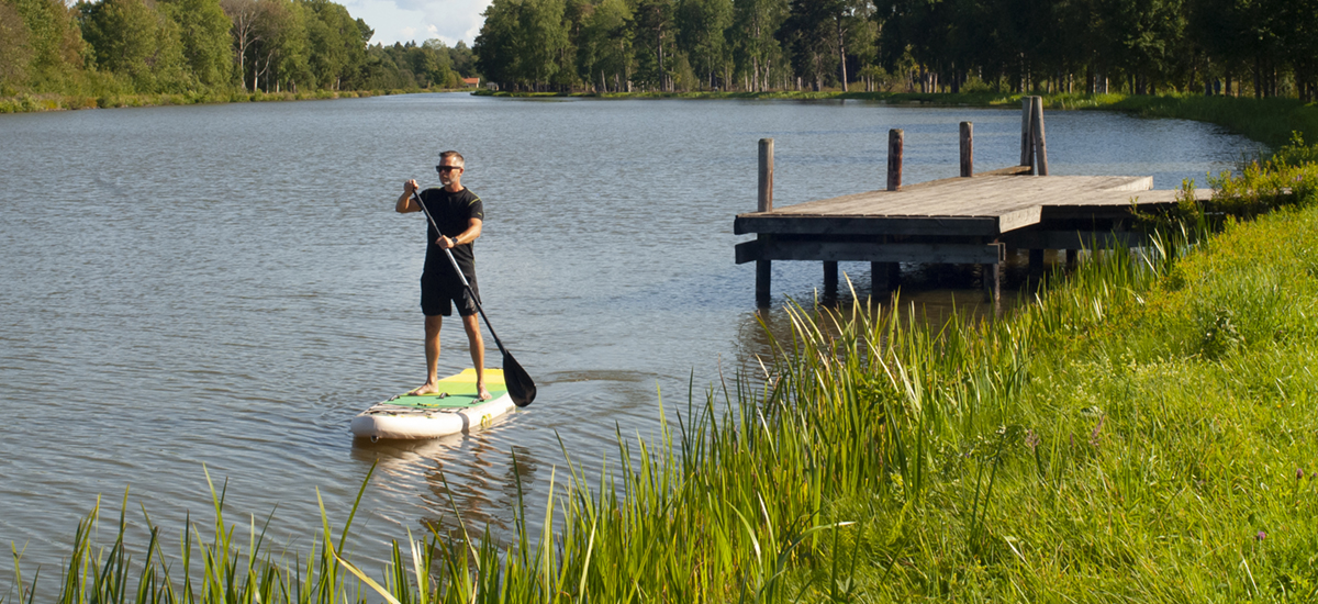 En man står på en SUP-bräda och paddlar i Göta kanal