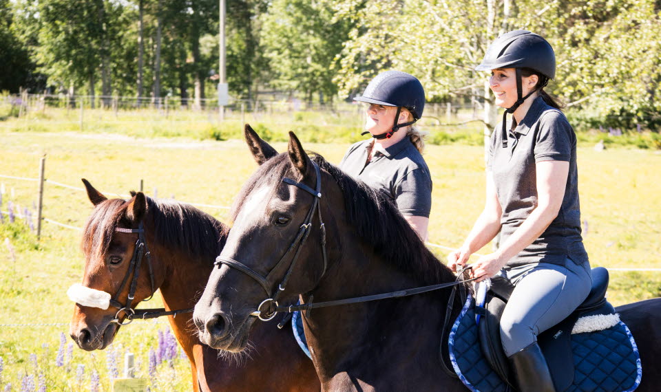 Två kvinnor rider utomhus.