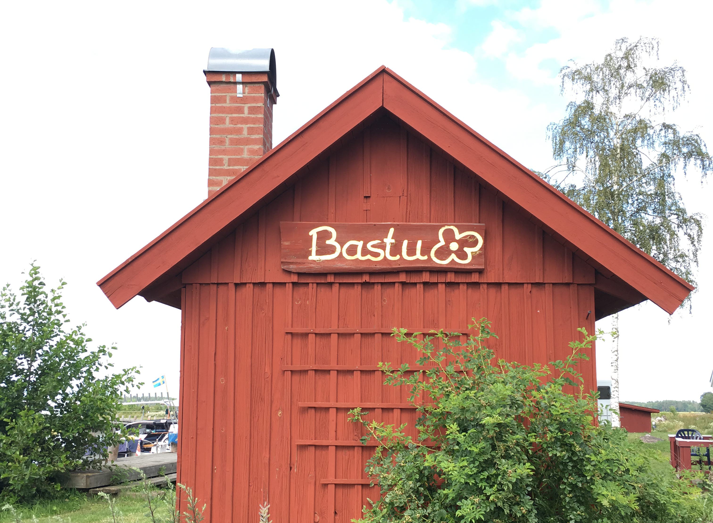 A small red house with a chimney and a sign that says bastu, meaning sauna.