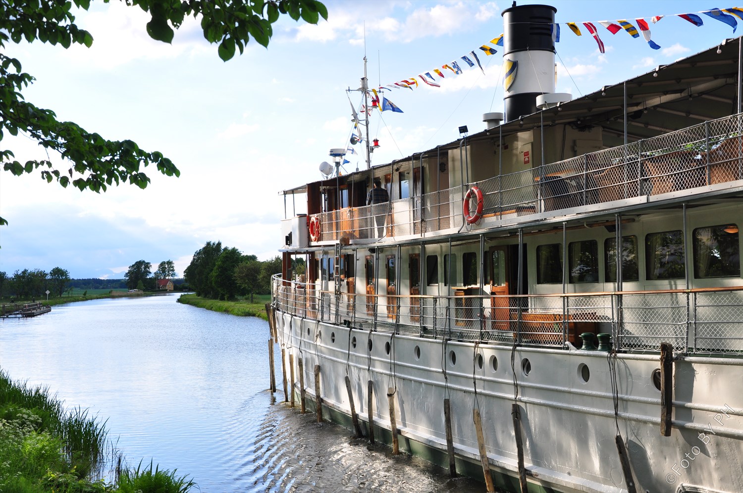 Vit passagerarbåt åker i Göta kanal en sommardag