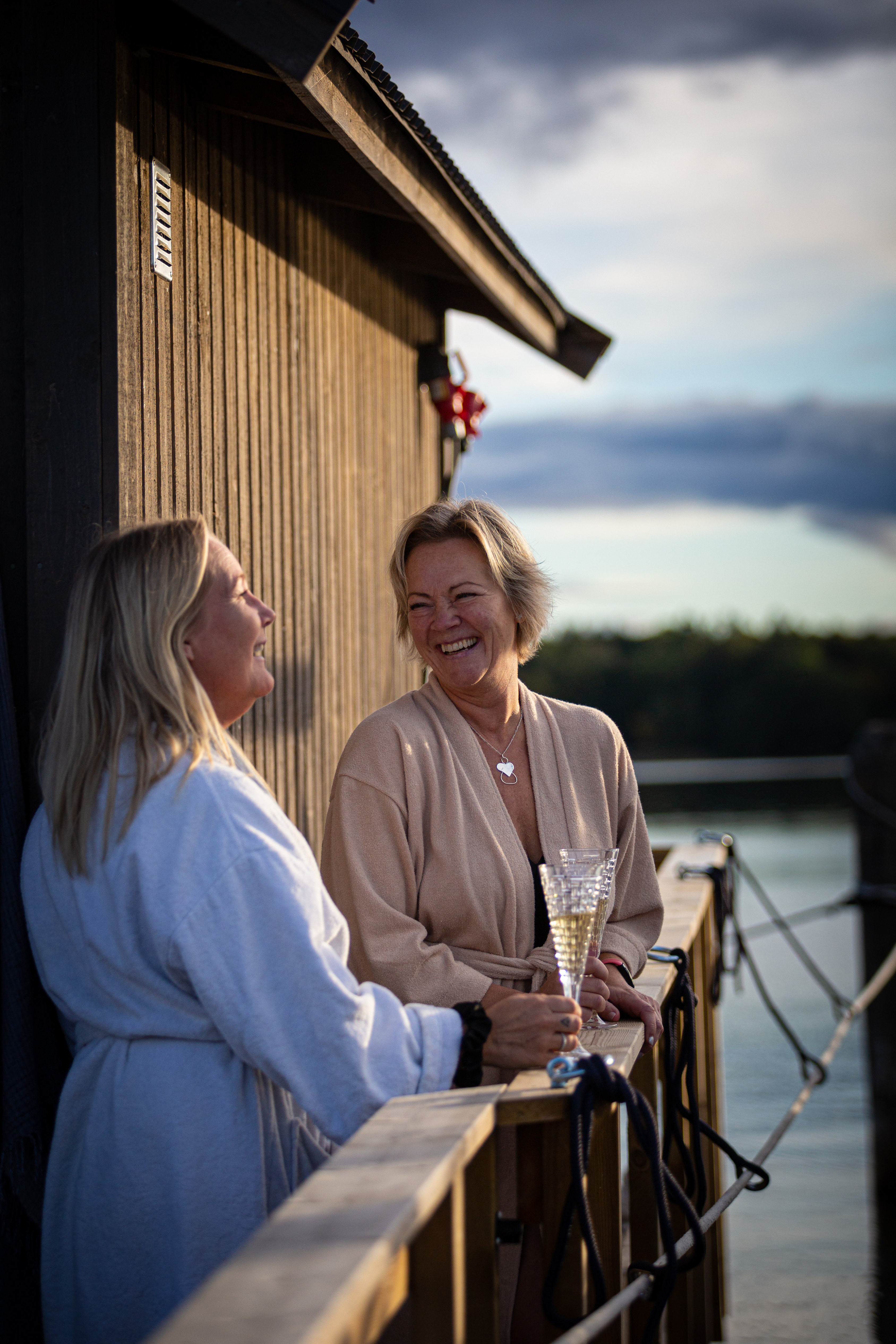 Två kvinnor pratar och skrattar med ett glas i handen på däcket av bastuflotten