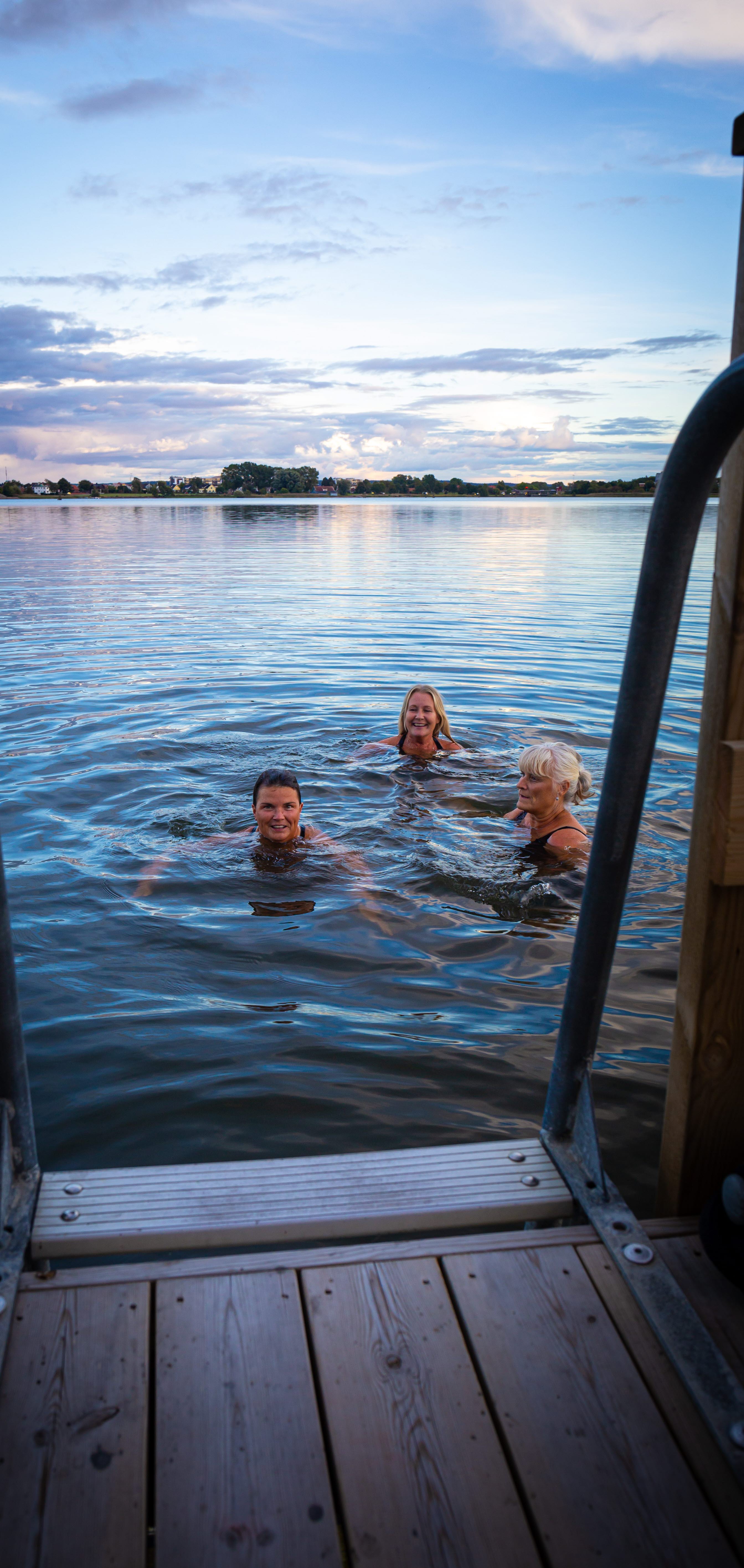 Tre personer badar i sjön från Bastuflotten 