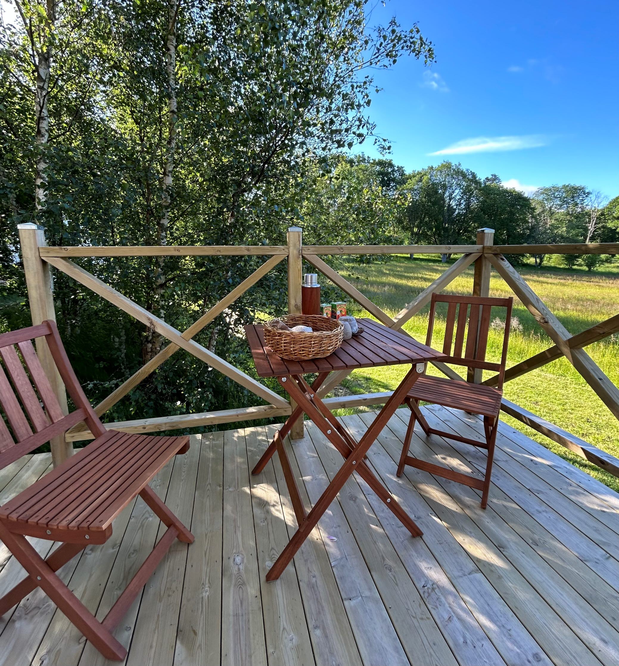 one table and two chairs on a wooden deck next to a meadow