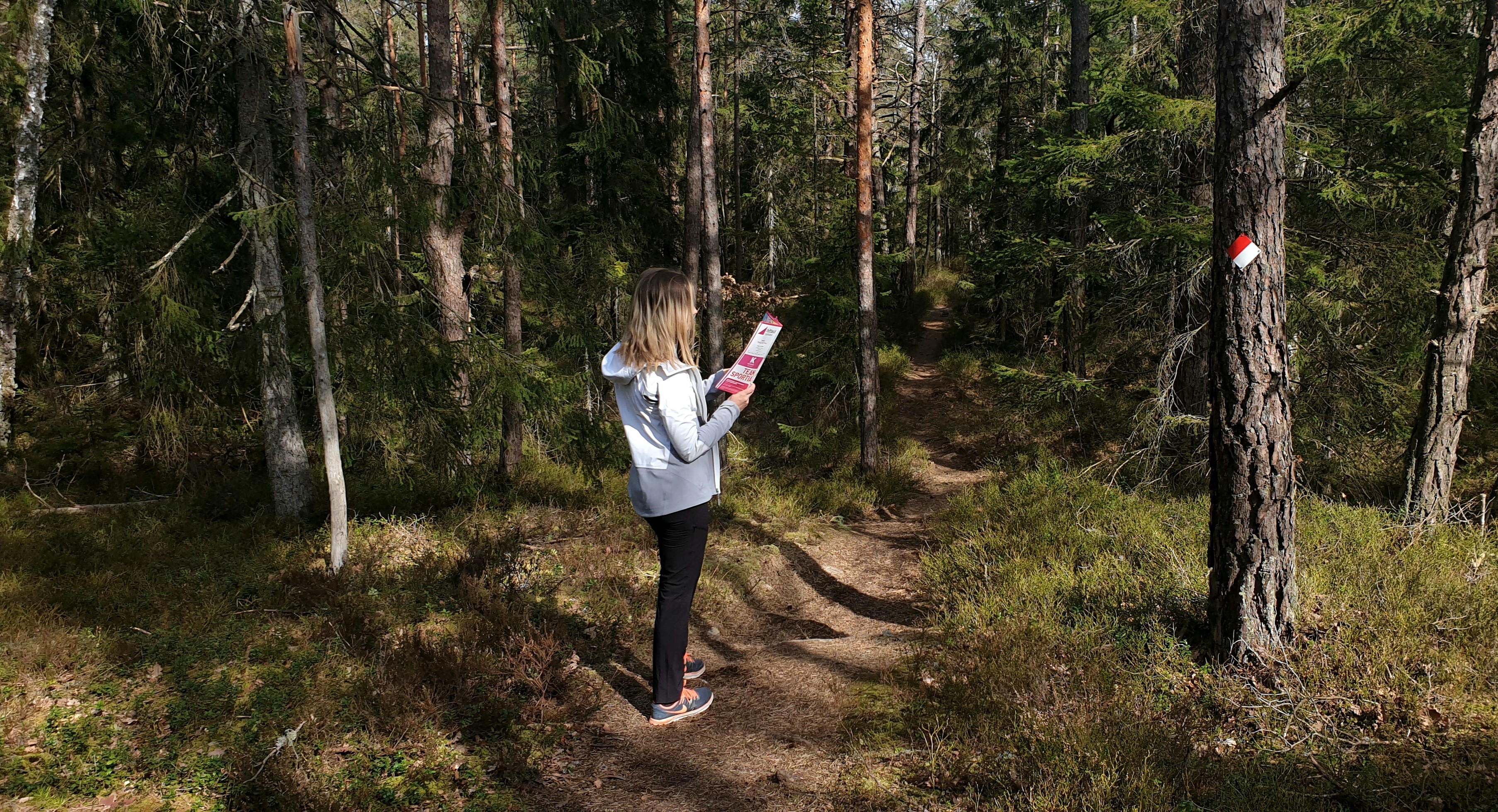 Person som står vid en stig och tittar på HittaUt-kartan.