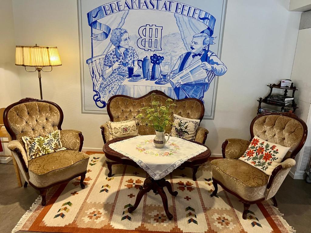 Tre fåtöljer framför en väggmålning med Hotell Beles logotyp