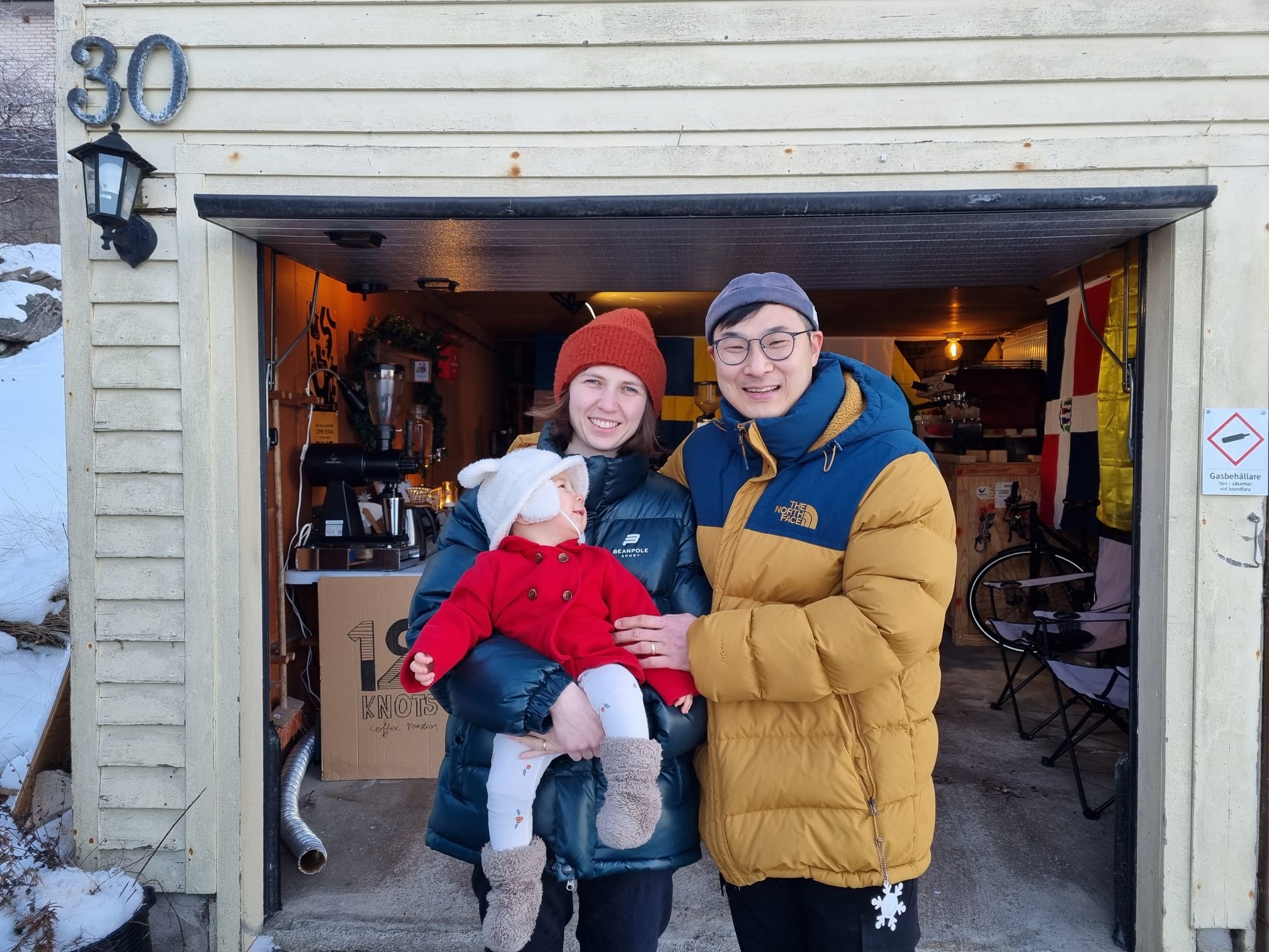 Two people holding a baby outside of a garage