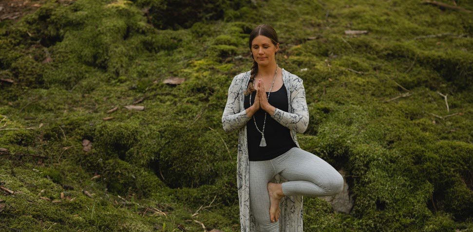 Kvinna står i yogapose barfota i naturen