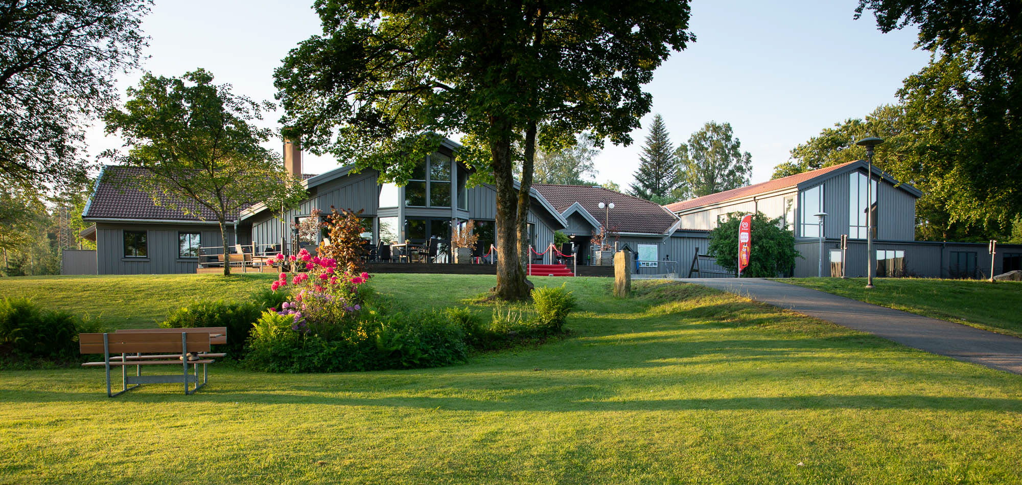 En gräsmatta med träd. Bakom träden finns ett hotell