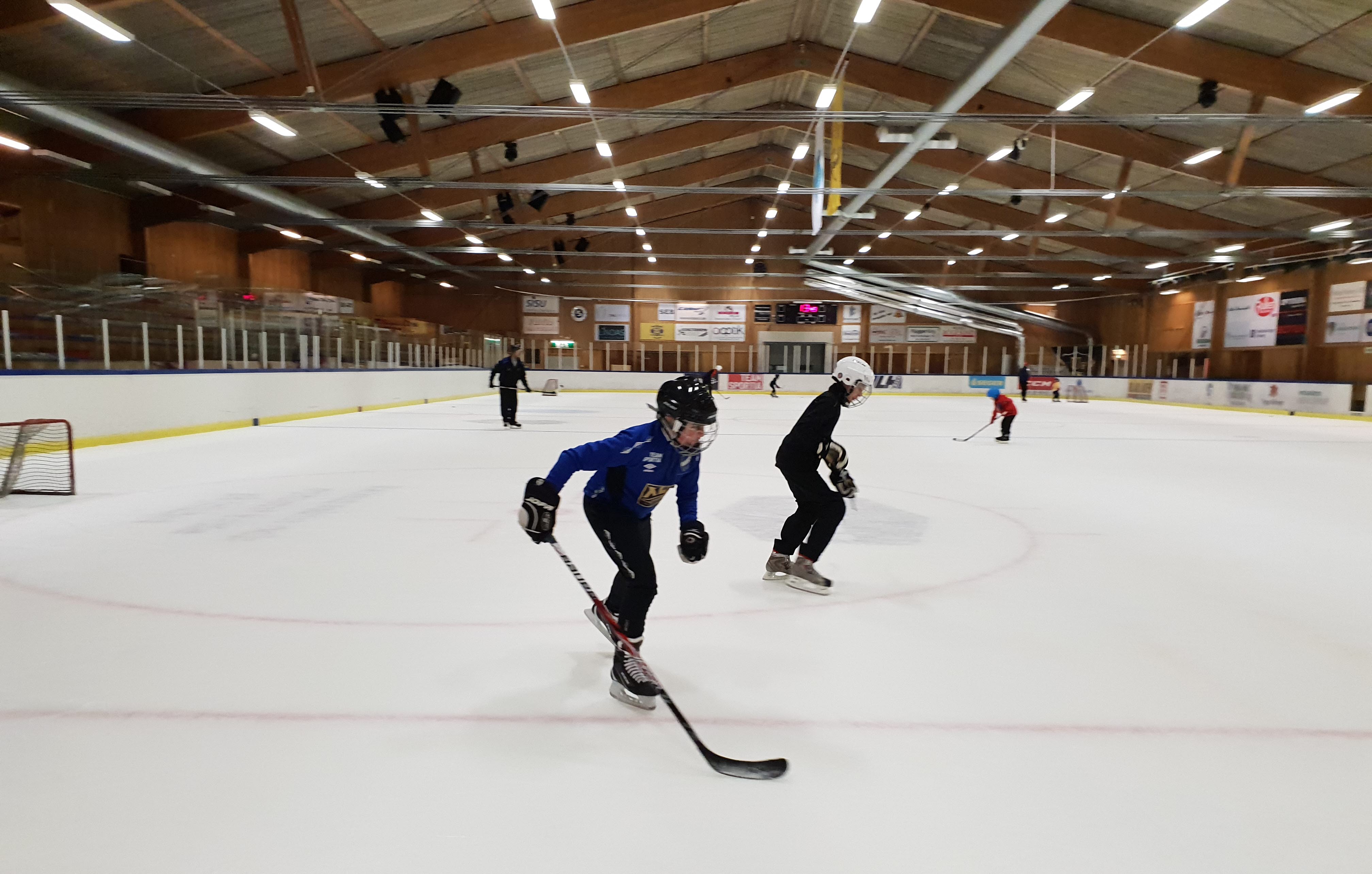 Two guys are skating in the ice rink. Both have a helmet and one of them has a hockey stick.