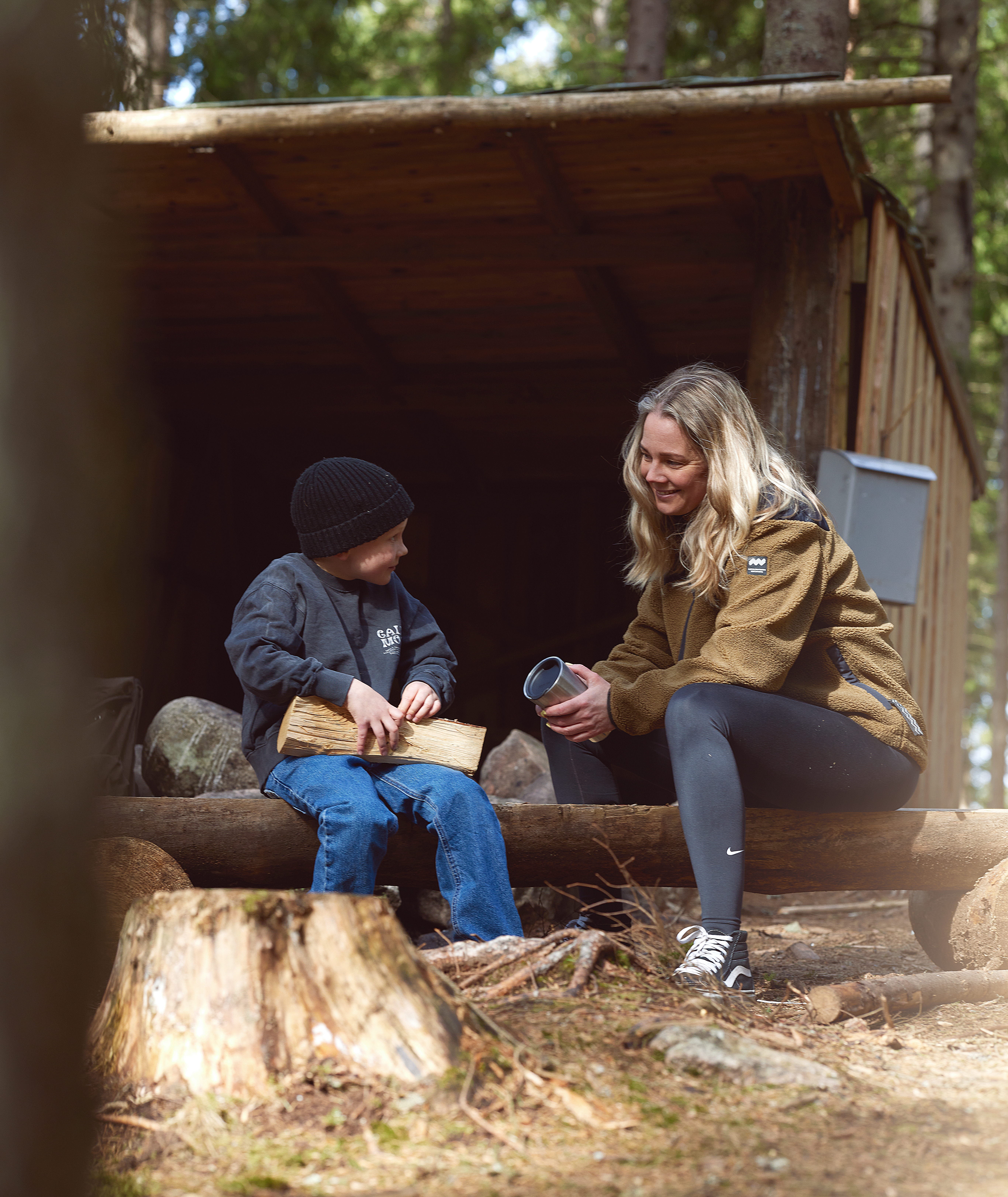 Mamma och barn sitter och njuter i höstvädret vid ett vindskydd