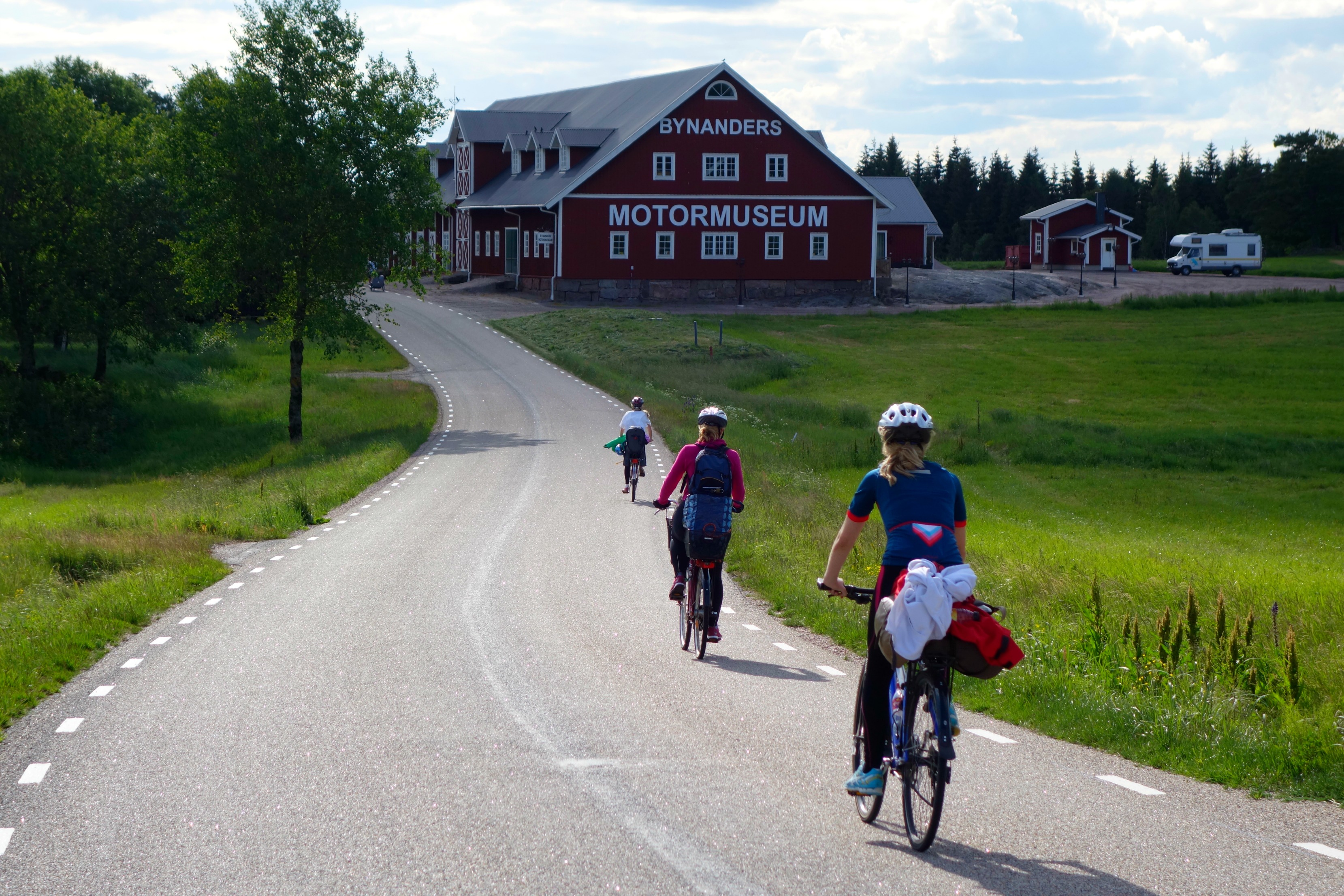 Personer cyklar på landsväg mot en stor röd byggnad