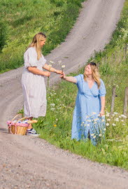 Två kvinnor som plockar blommor längs en grusväg vid Kärråkra kyrka i Sjuhäradsbygden. 