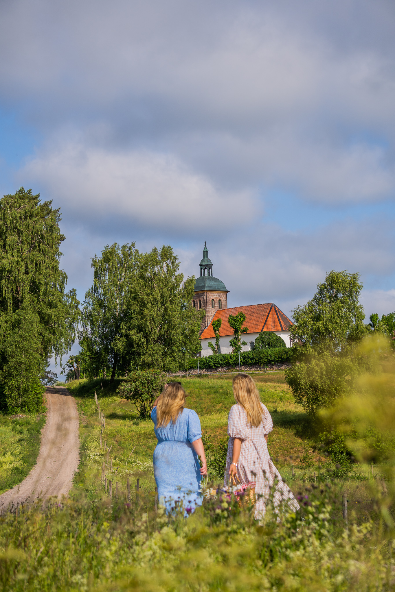 Två kvinnor klädda i sommarklänningar som tittar ut på en äng och en kyrka.
