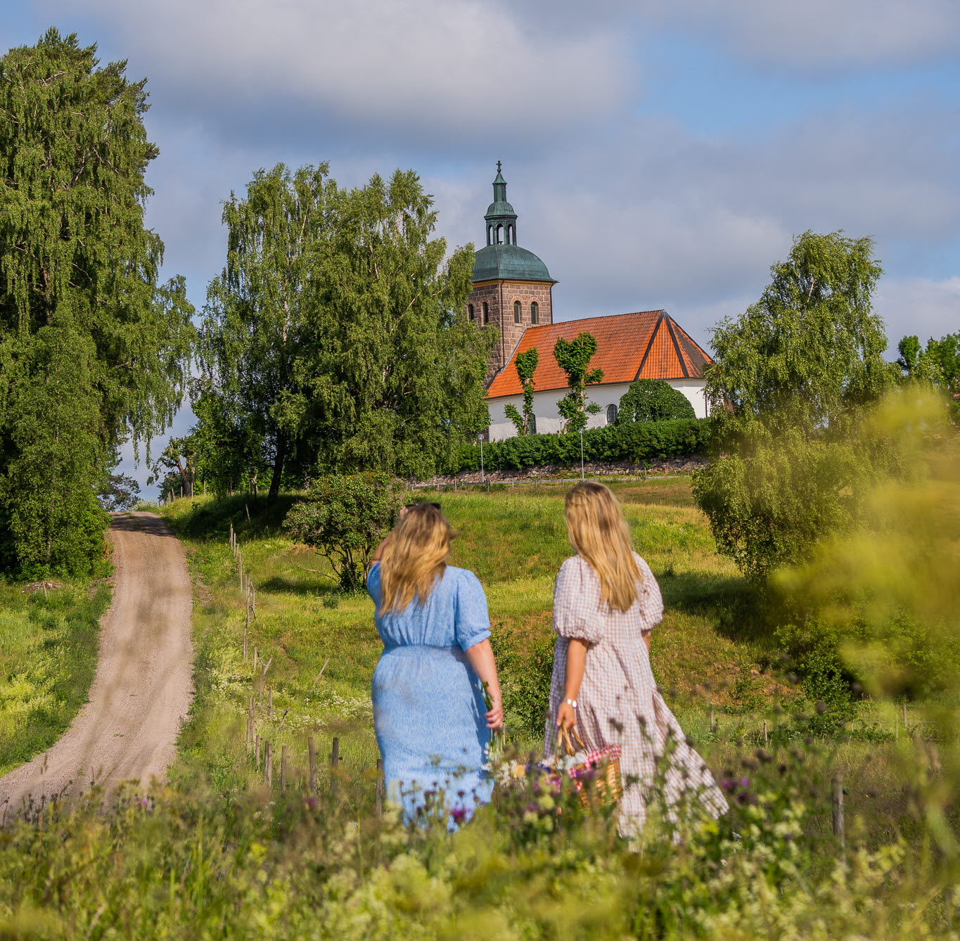 Två kvinnor som står i klänning och tittar på en kyrka på en liten grusväg.