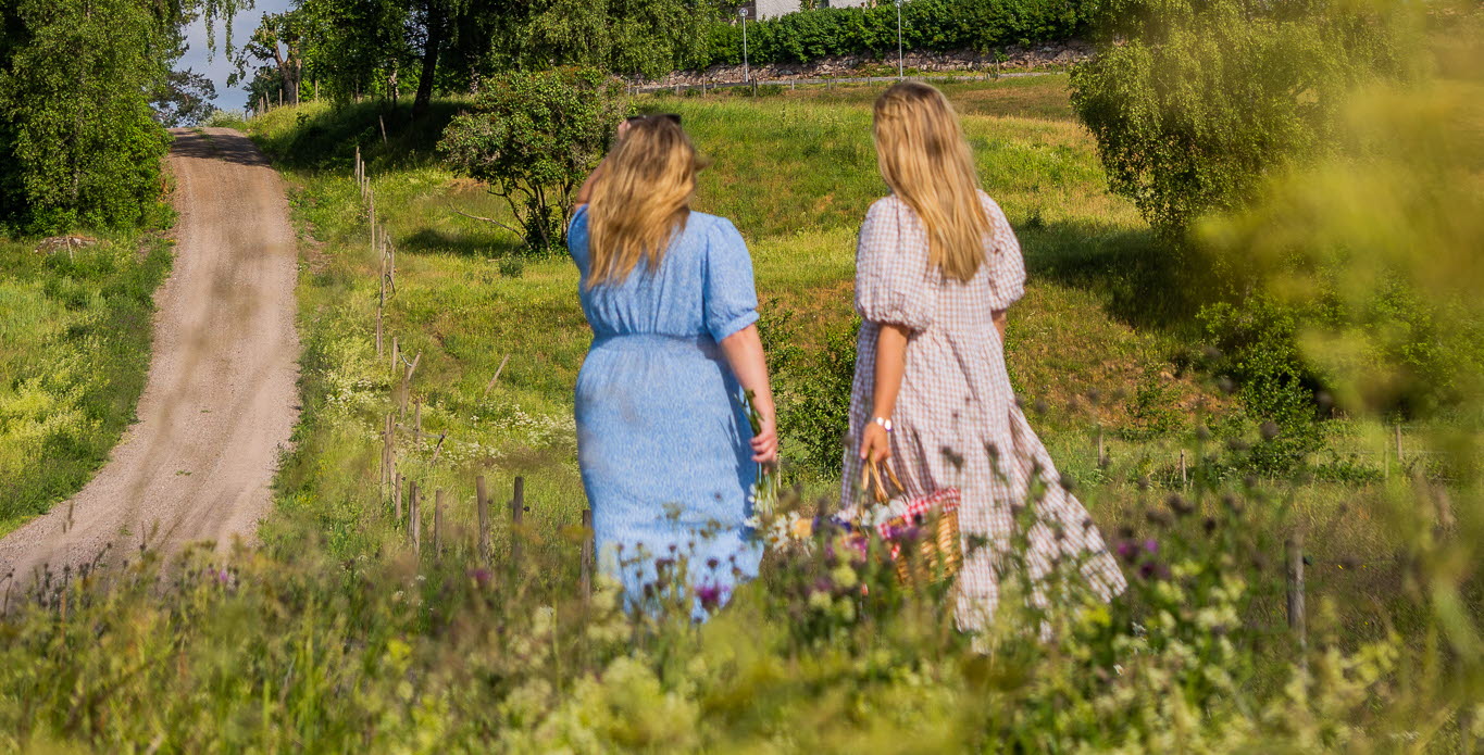 Två kvinnor som står i klänning och tittar på en kyrka på en liten grusväg.