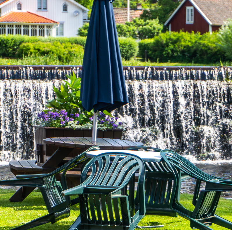 Bild på en bro vid ett kafé. Bron går ut till en liten ö i en å.