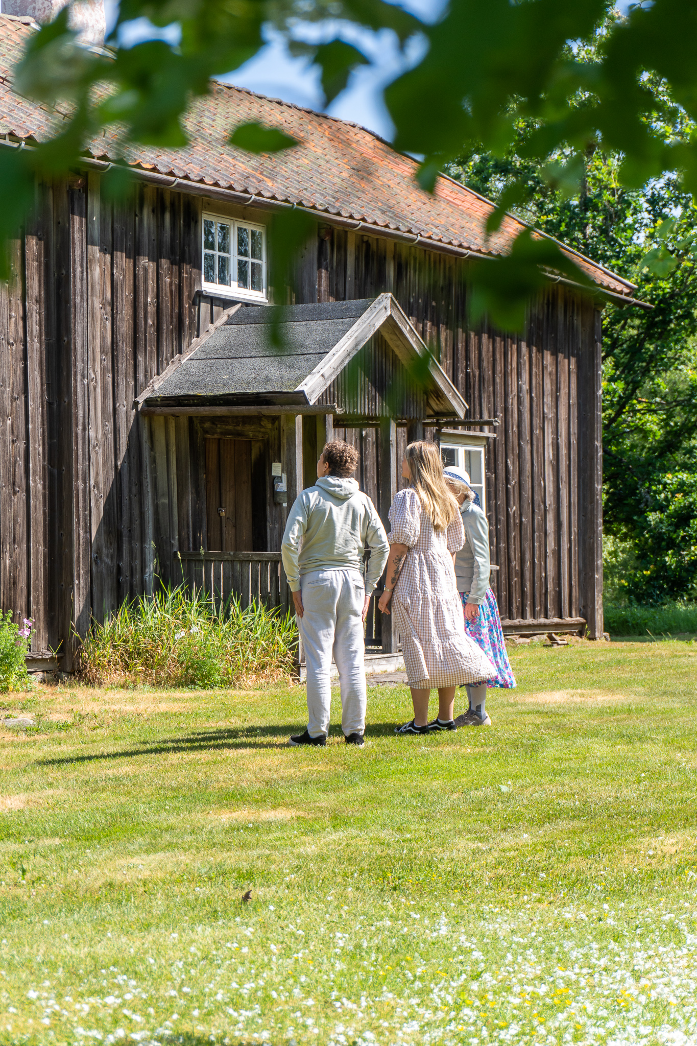 En tonårspojke och två kvinnor tittar på en restaurerad gård från 1800-talet.