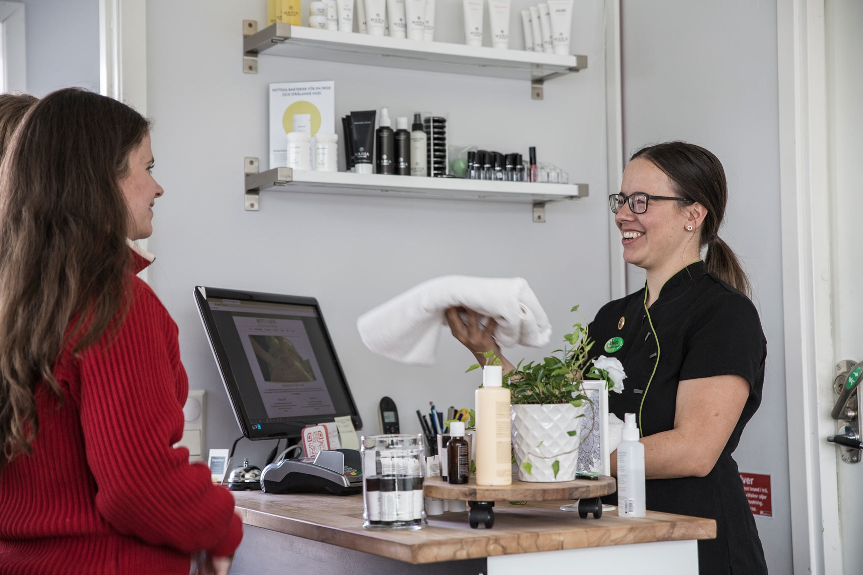 Två kvinnor vid en receptionsdisk ler mot varandra